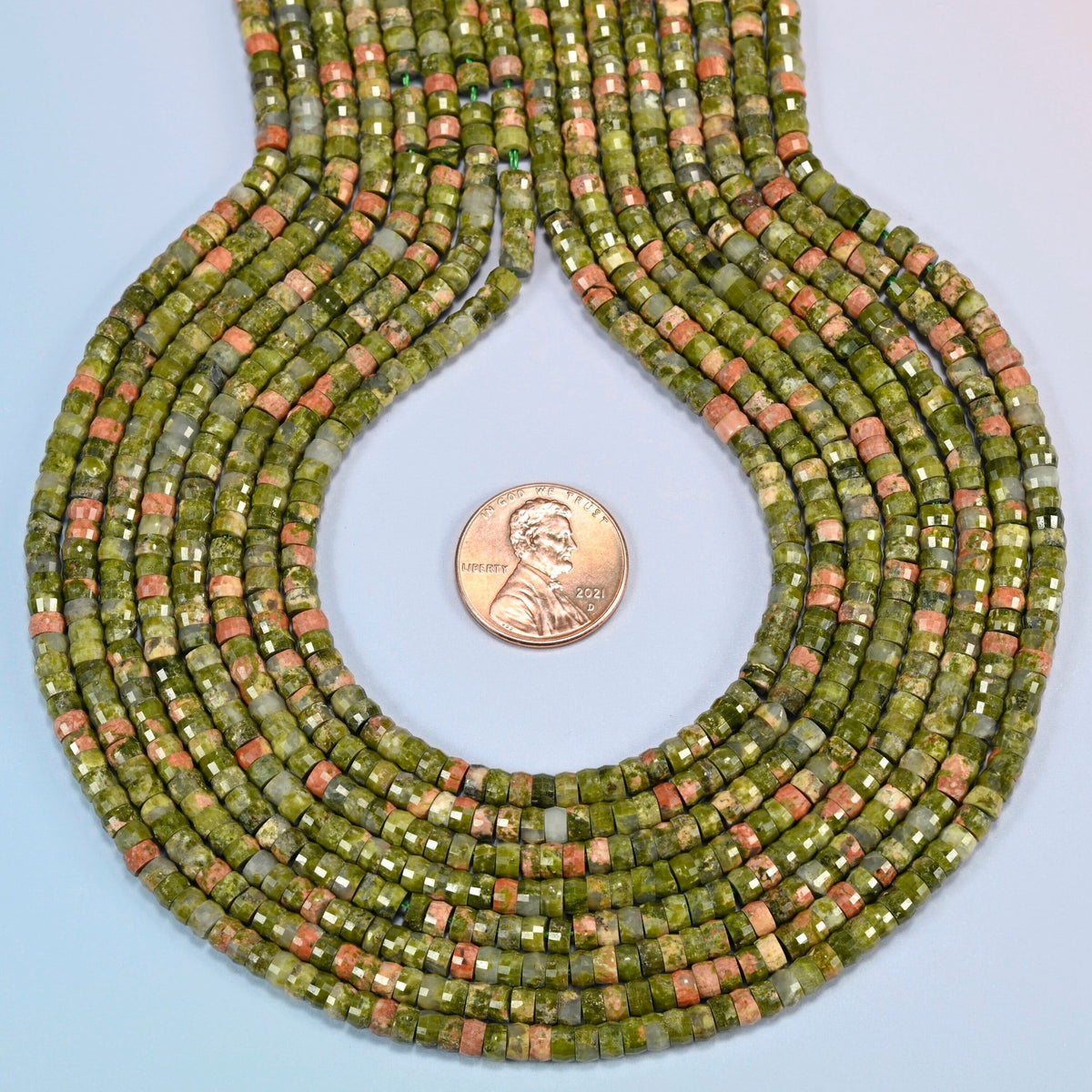 Unakite faceted heishi disc strands formed into a teardrop loop around a US penny for scale