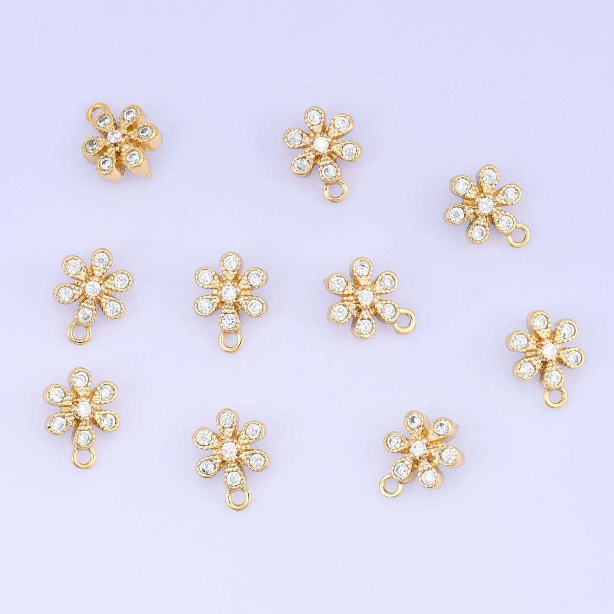 Small gold charms, eleven gold plated flower charms with clear cubic zirconia scattered on a pale backdrop