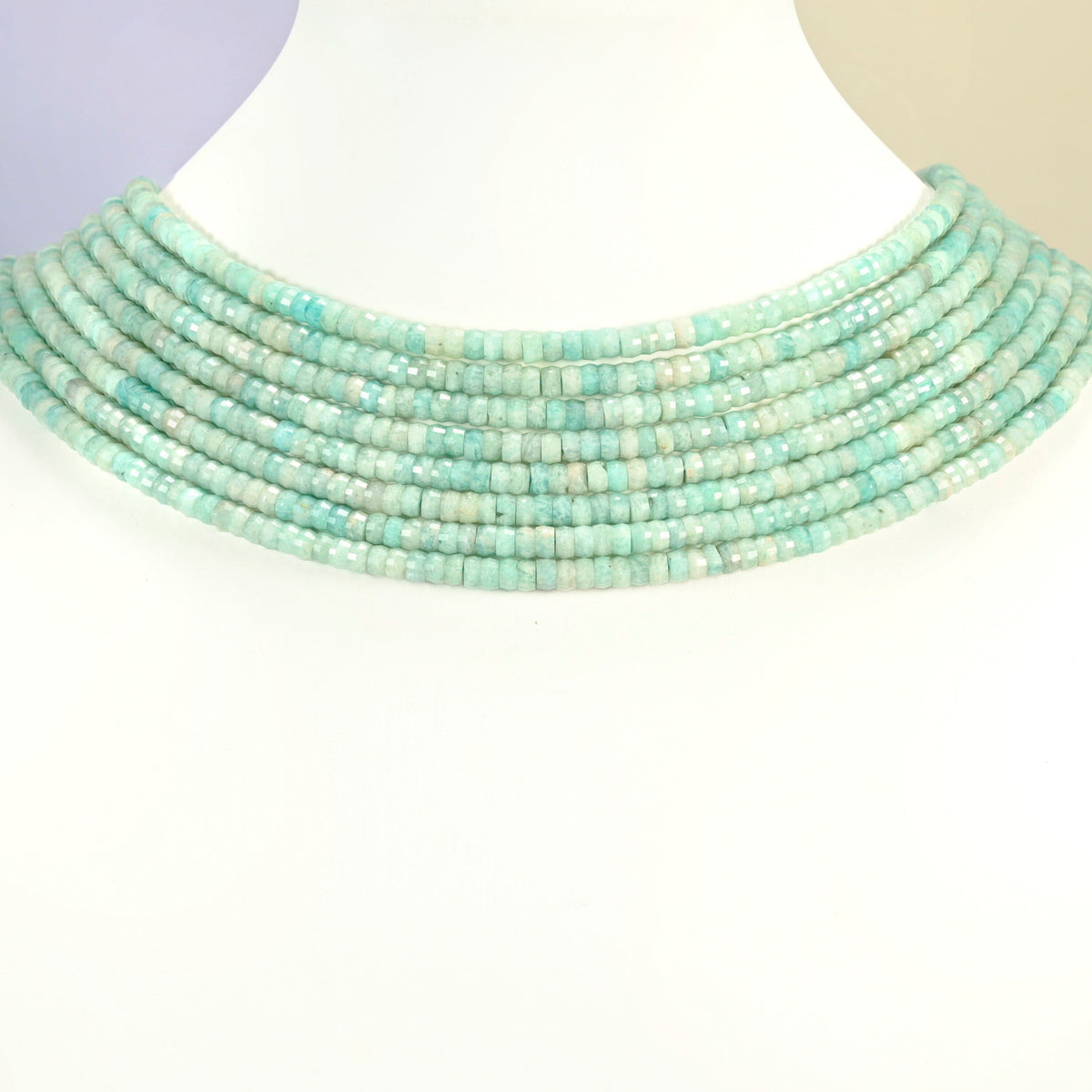 Green amazonite faceted heishi disc strands arranged as a layered collar on a white display bust, light green beads across the neck
