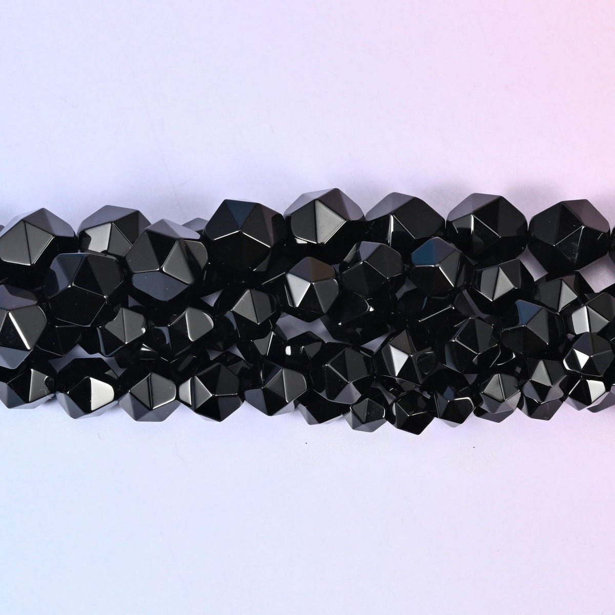 Black Onyx faceted beads close up in a single row, flat triangular star cut planes on a glossy black finish