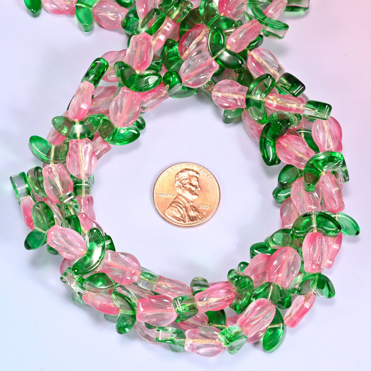 Horizontal row of pink tulip and green leaf glass beads laid straight across a lavender background, showing the alternating flower and leaf pattern.