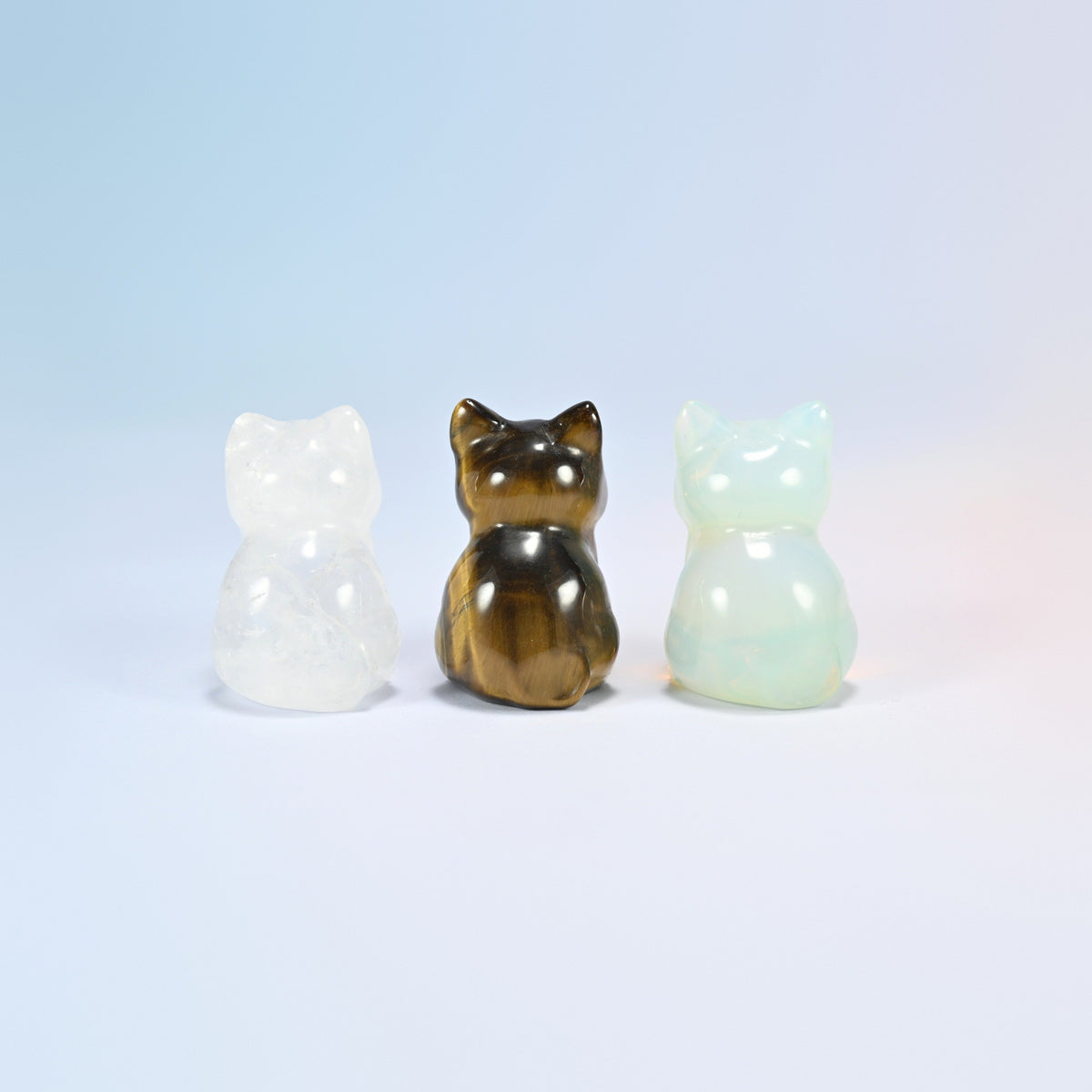 Back view of three sitting cat gemstone carvings in clear, brown and milky white
