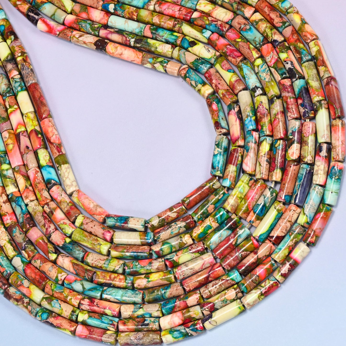 Top-down view of jasper tube bead strands arranged in a loose spiral on a lavender background, highlighting the mix of colors and stone texture.