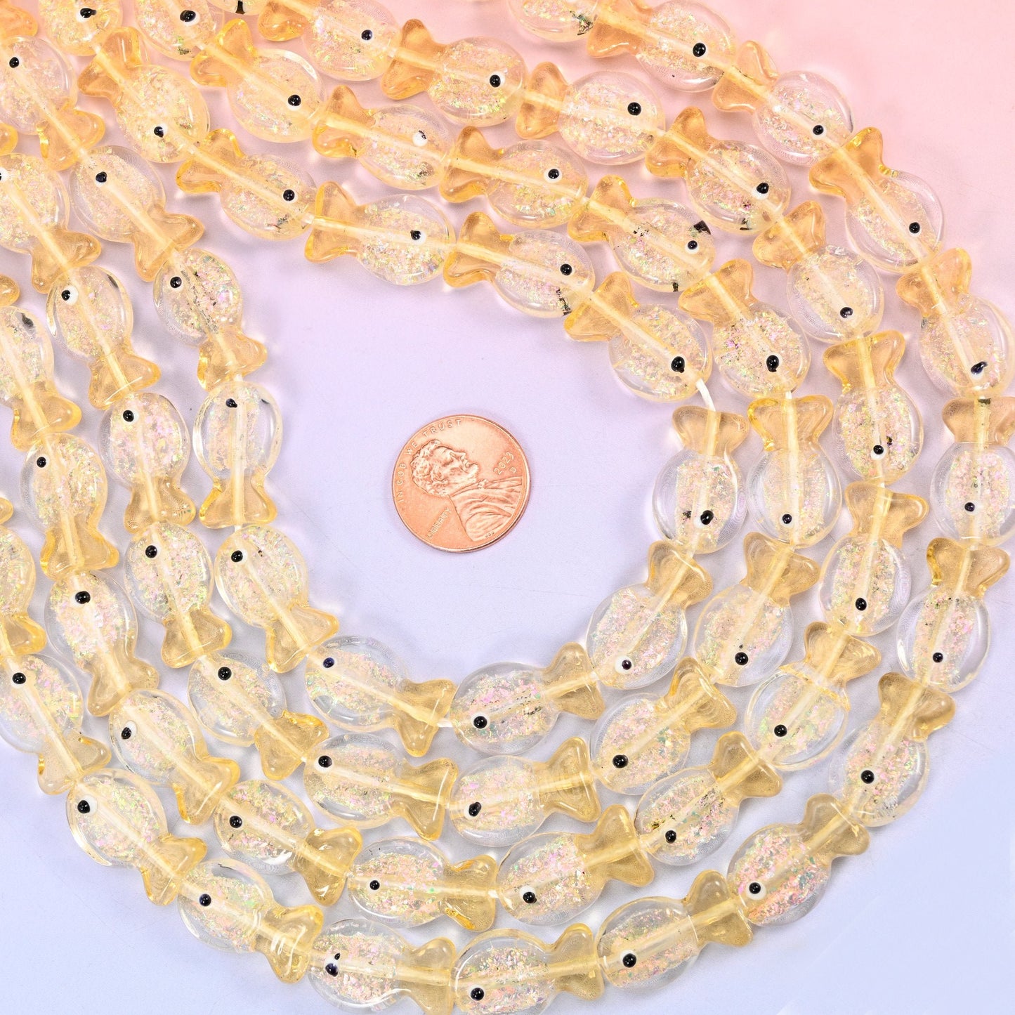 Iridescent Yellow Fish Glass Beads — little lampwork fish in clear butter-yellow glass with gold glitter suspended inside the body and a single black dot for the eye.