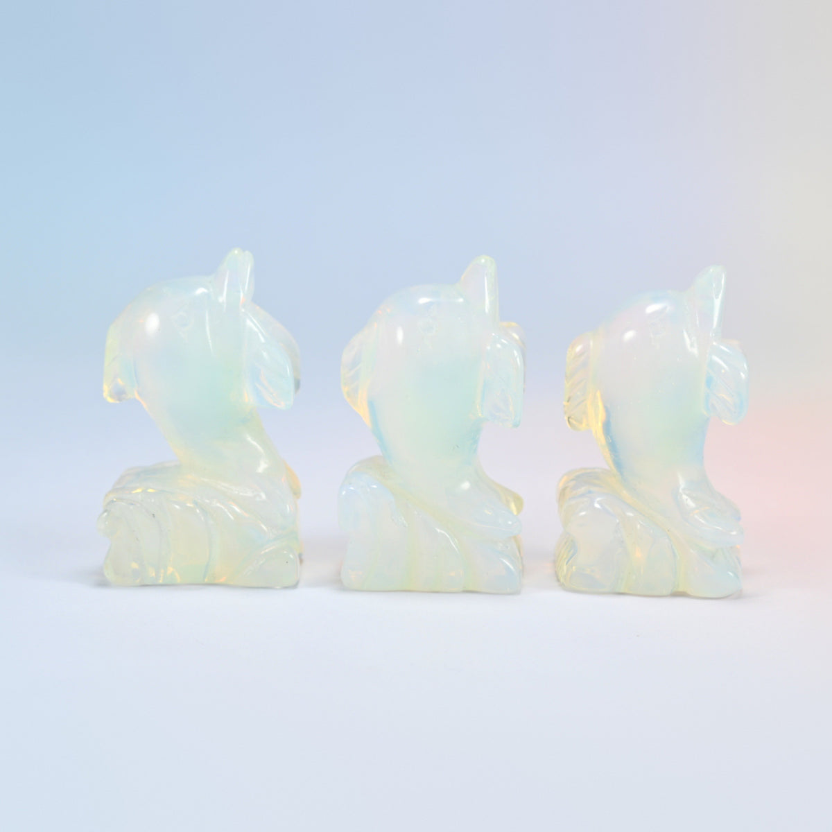 Three glowing opalite dolphin carvings turned at an angle