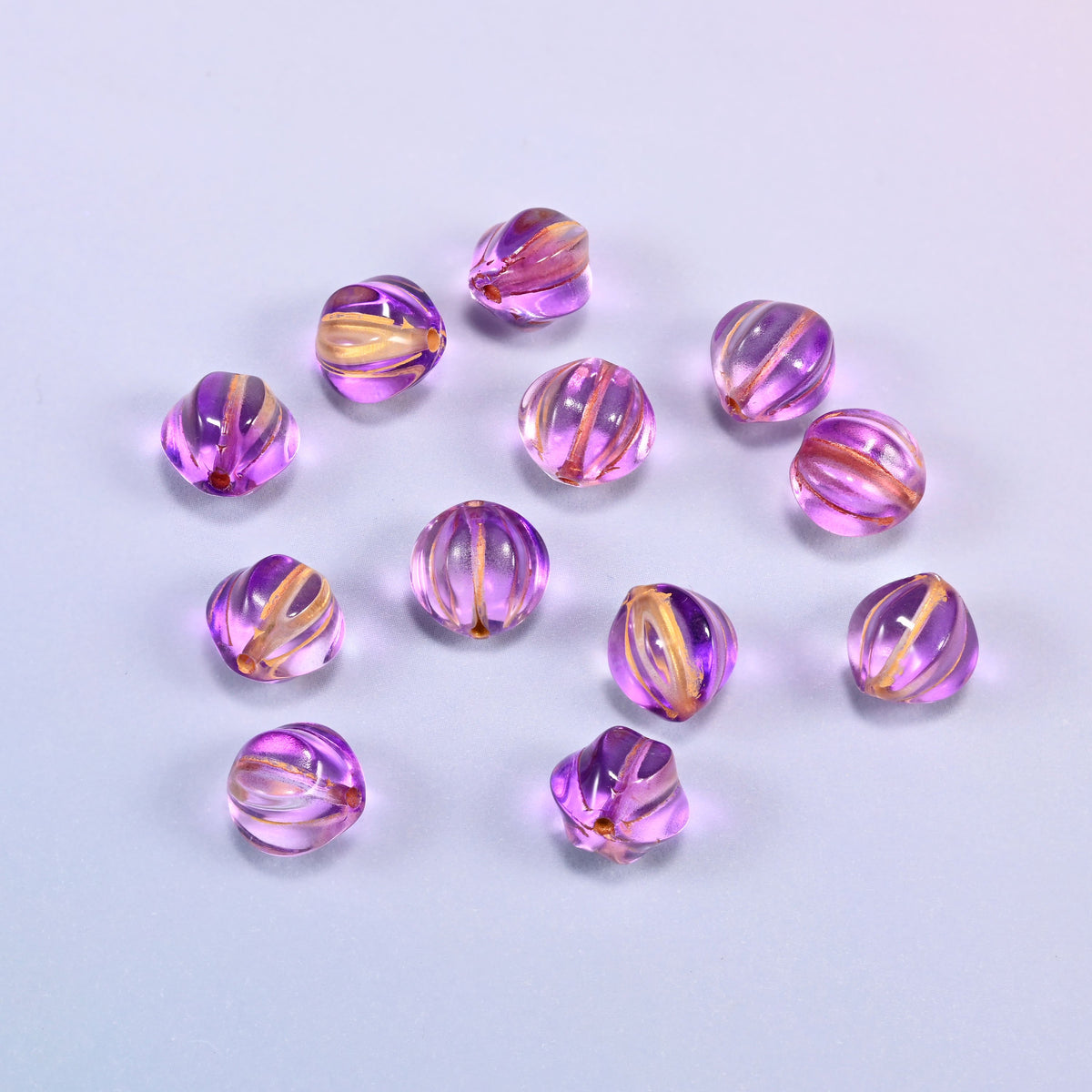 A scattered group of loose 8mm purple gold pumpkin glass beads, showing the melon ribs and the drill holes.