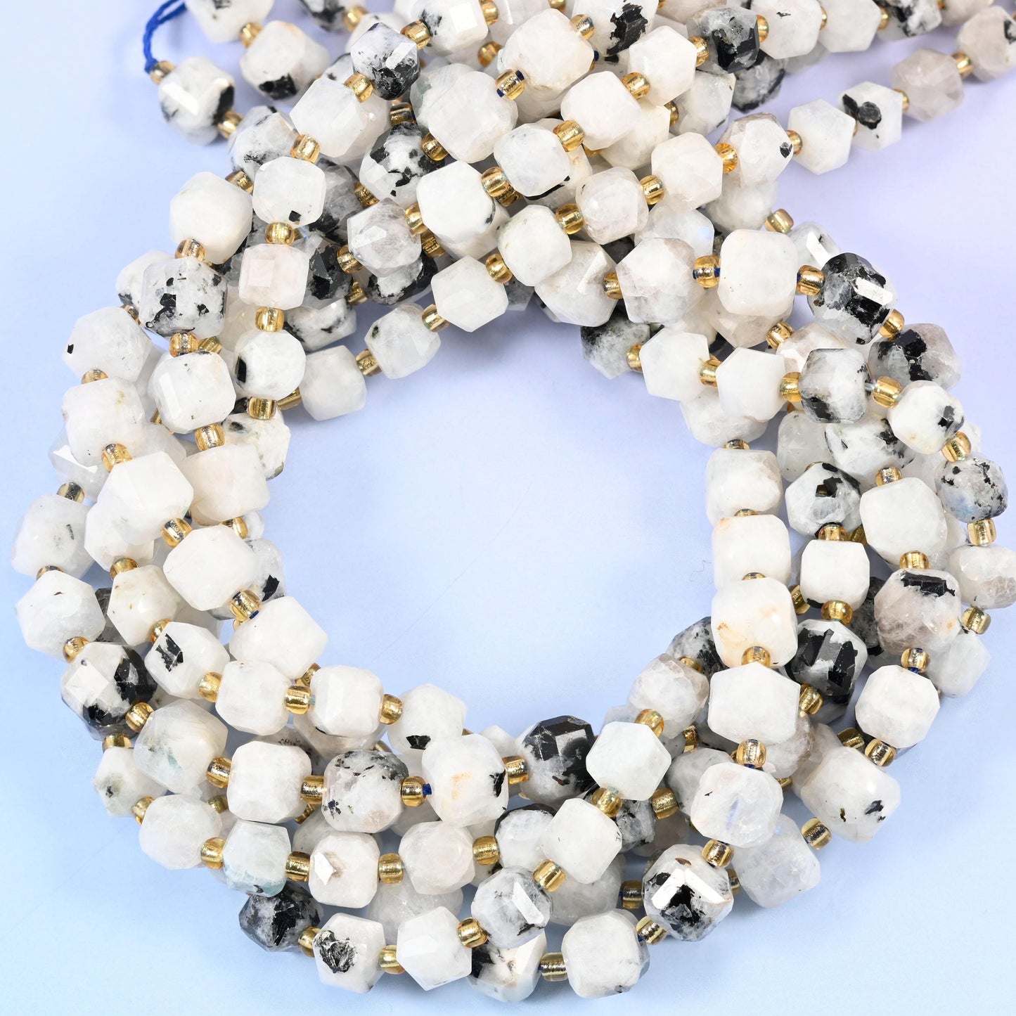 Milky white cubes blotched and flecked with charcoal black, corners cut into facets so light breaks across the flat faces. Despite the Blue Moonstone name these read white and grey in hand, not blue.
