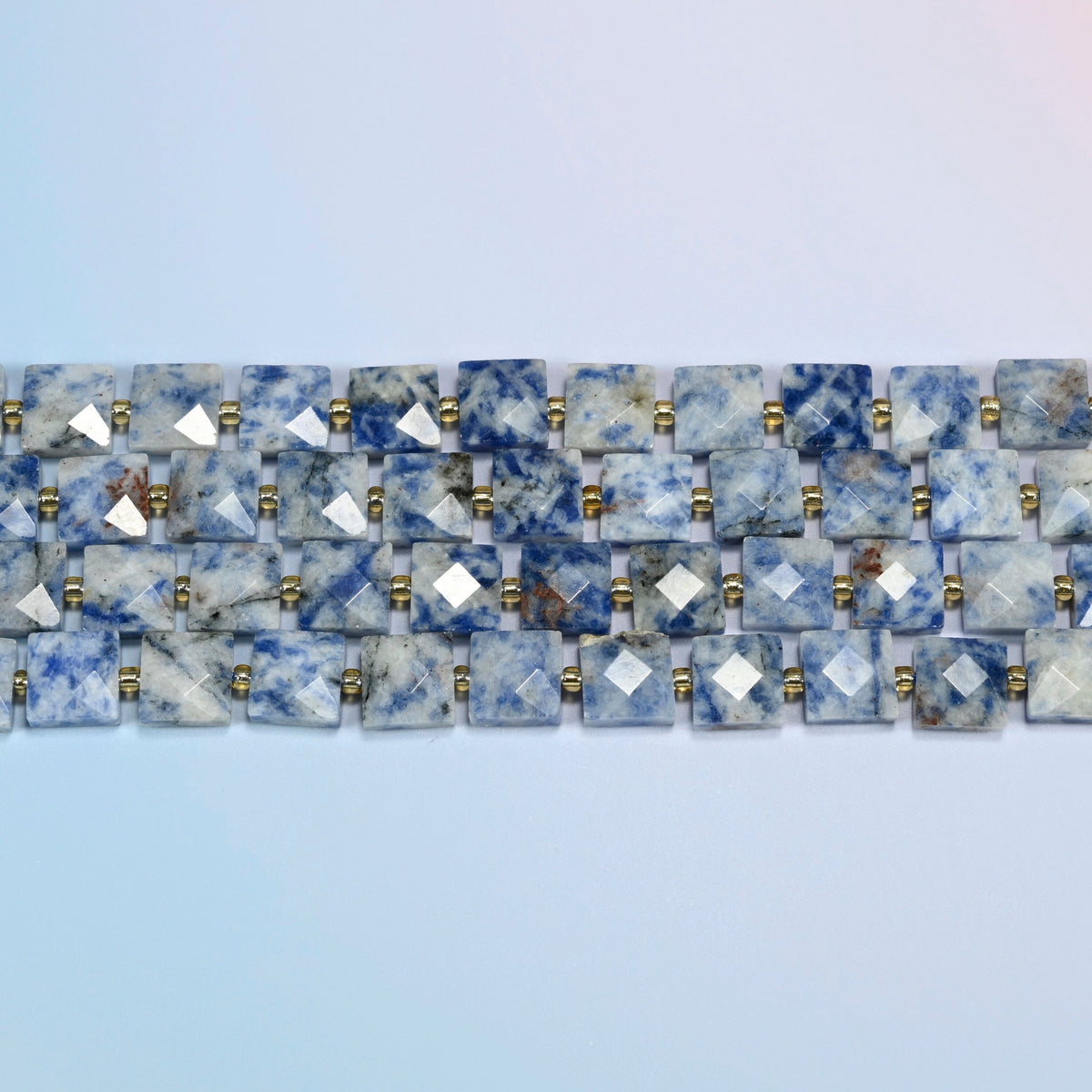 Several strands of natural blue spot jasper faceted flat square beads laid in straight rows