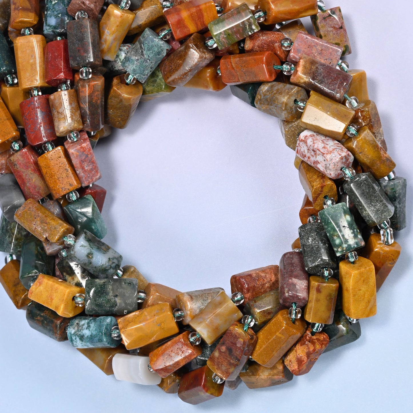 Close-up horizontal row of faceted Ocean Jasper tube beads showing the multicolor stone pattern and clear glass spacer beads.