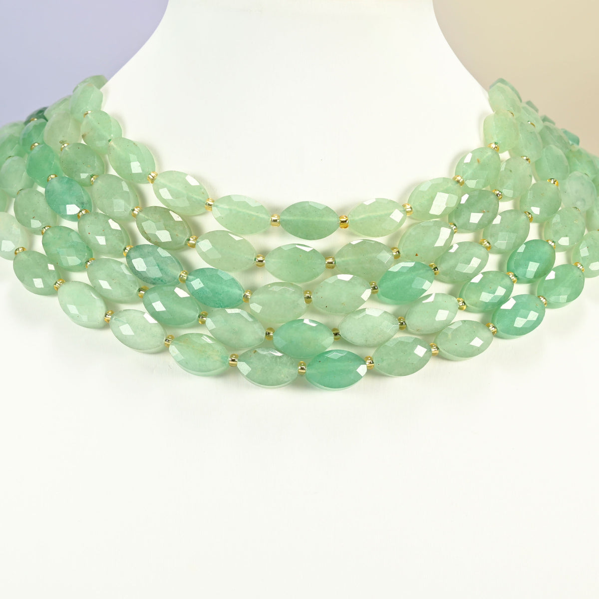 Green aventurine faceted flat oval strands arranged as a layered collar on a white display bust, mint green beads across the neck
