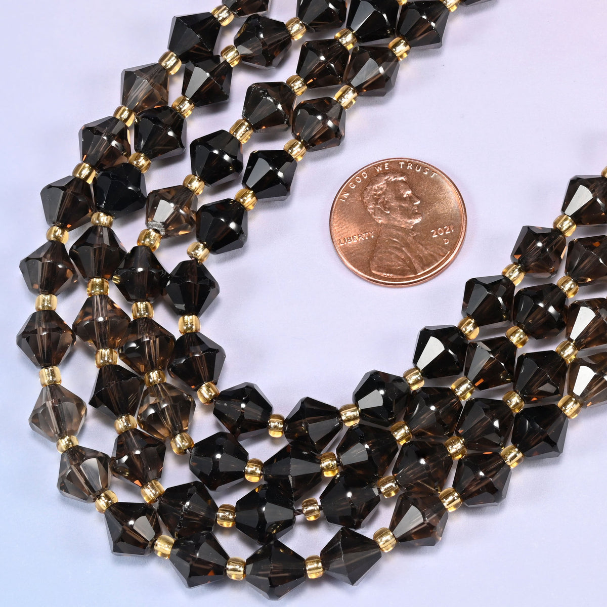 8mm Smoky Quartz faceted bicone beads coiled into a loose circle on a light lavender background.