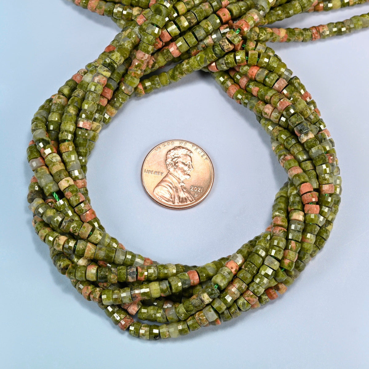 Unakite faceted heishi disc beads 2x4mm coiled in a loop around a US penny for scale, close-up of the faceted disc shape