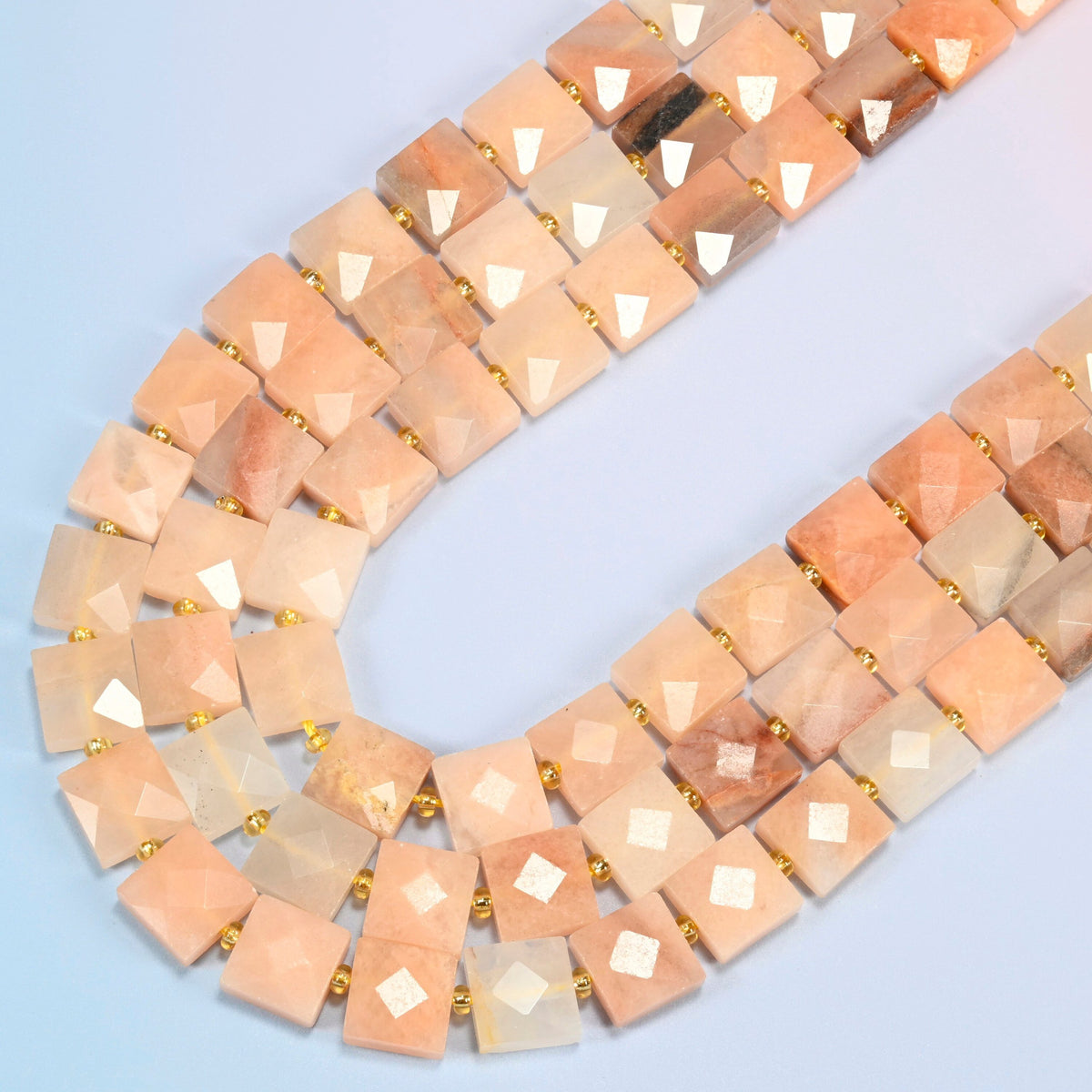 Natural pink aventurine faceted flat square beads in several strands curved into a wide U, light peach pink stone