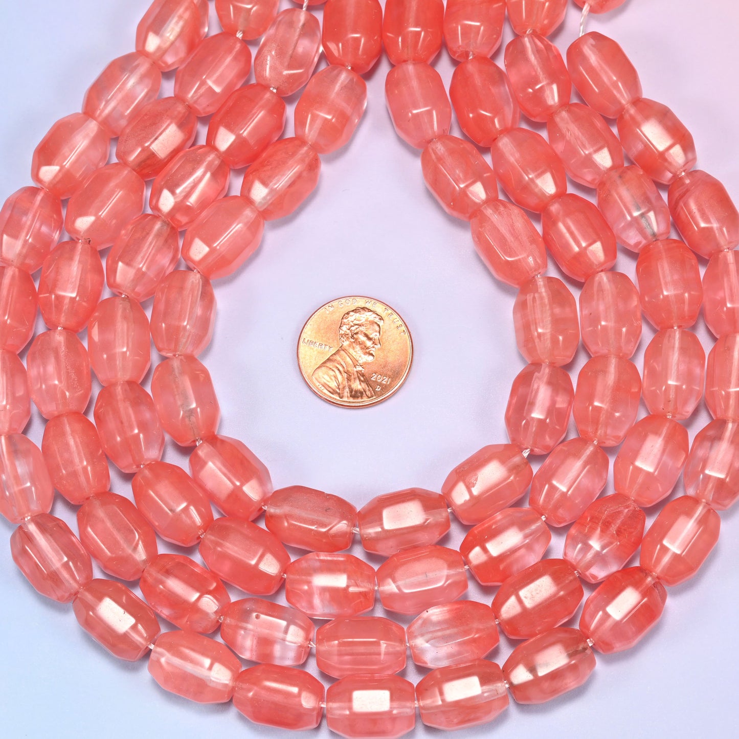 Wide circular coil of faceted glass barrel bead strands on a light background with a penny in the center for size comparison.