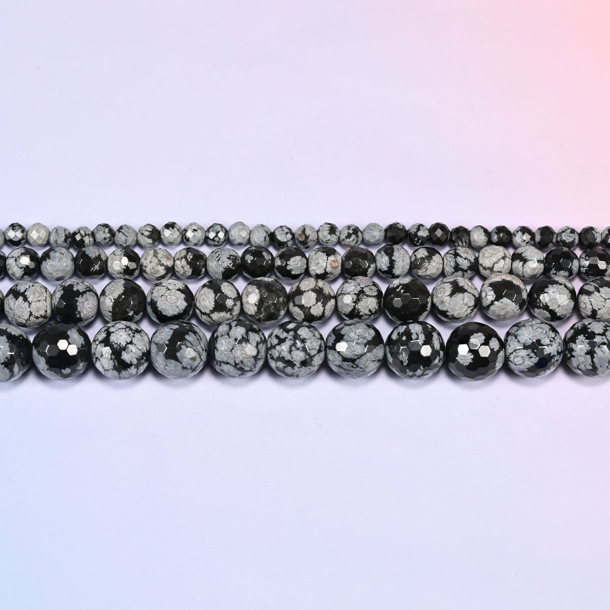 Three rows of Snowflake Jasper faceted round beads laid side by side, showing the graduating sizes and the stone's black and gray snowflake pattern.