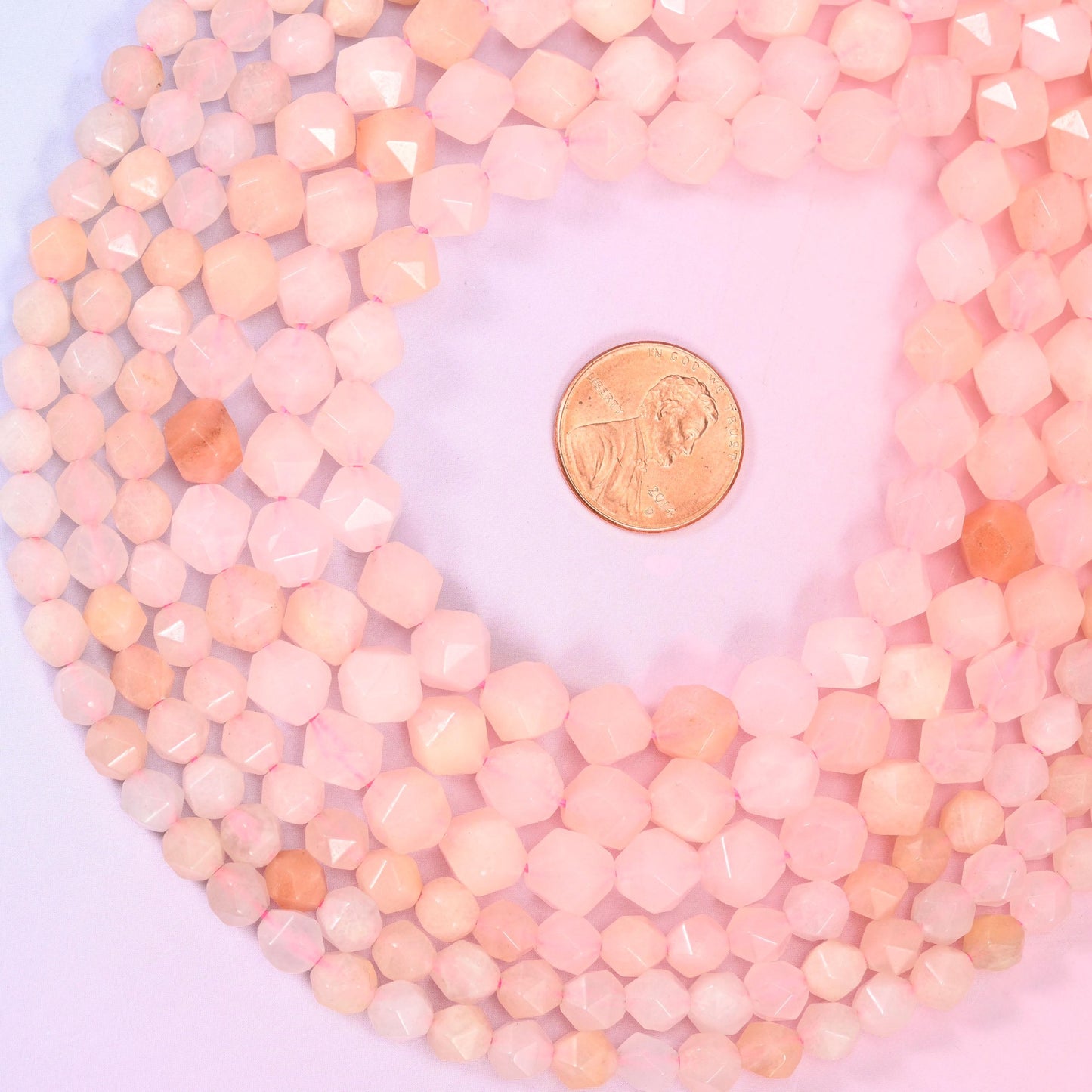 Pink Aventurine diamond star cut beads coiled around a US penny for size reference, centre drilled
