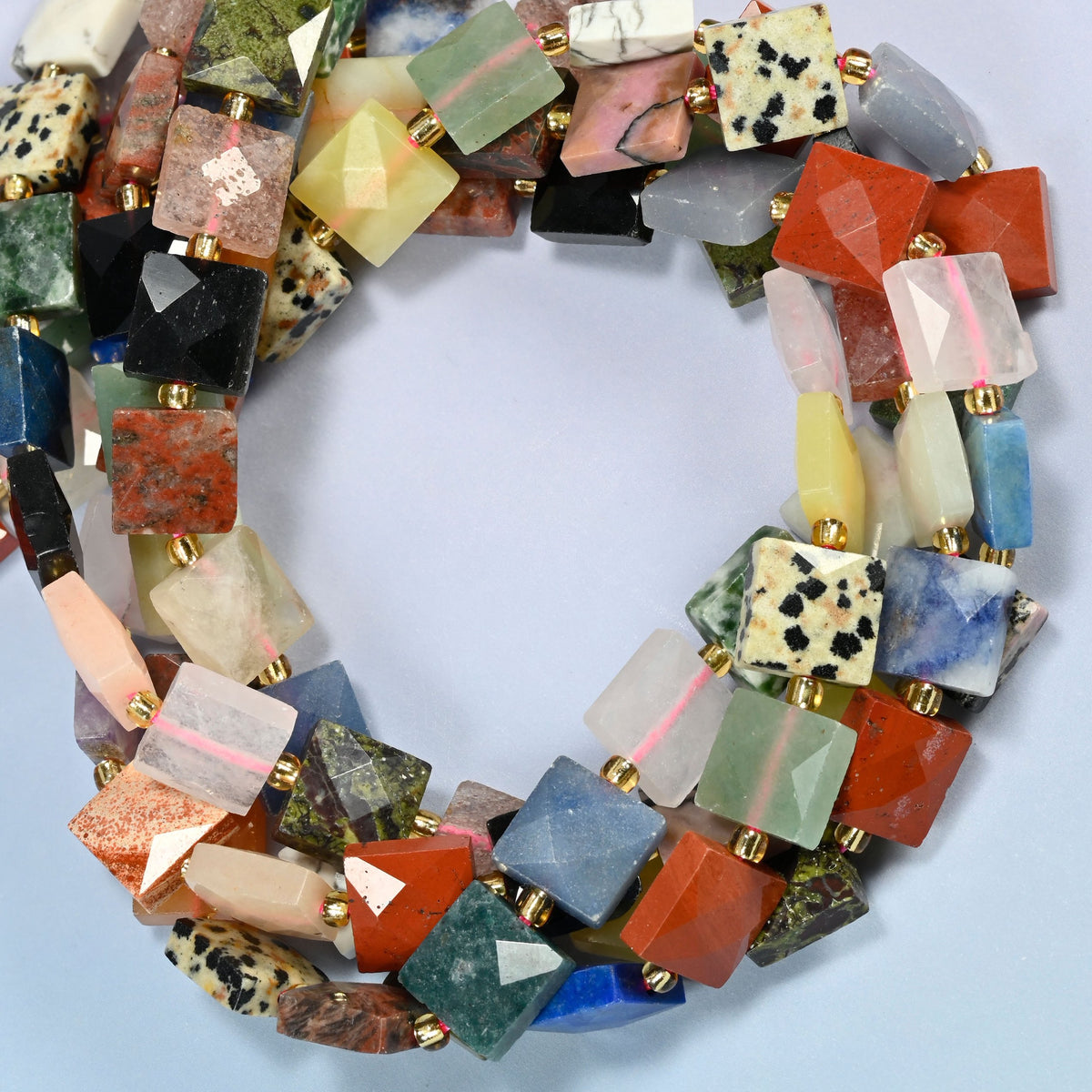 Assorted gemstone faceted flat square beads coiled into overlapping loops, whole strands of stones in a rainbow of colors