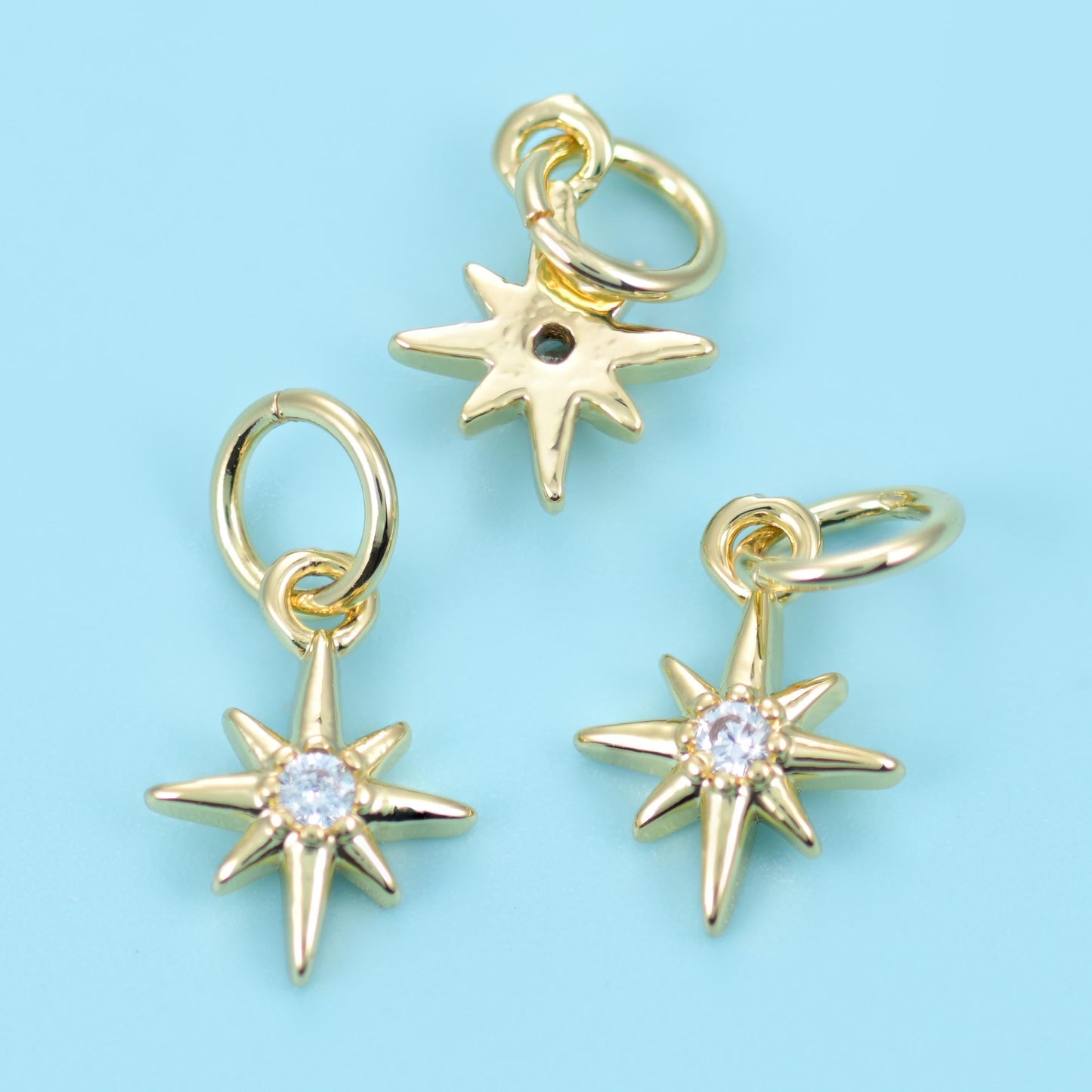 A slim eight-point star with long tapered rays and a bright round zircon set at the centre, finished in warm polished gold…