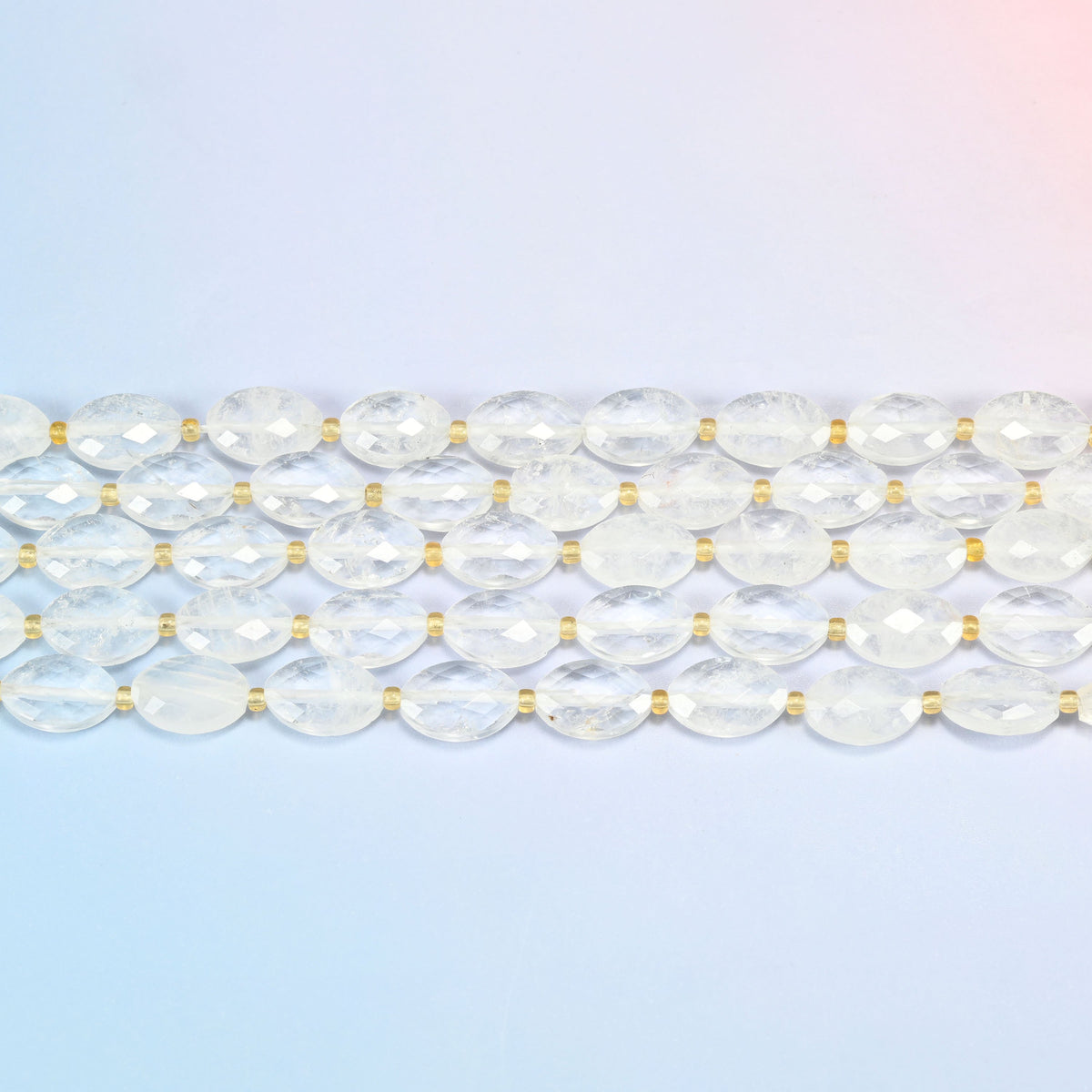 Several strands of clear quartz faceted flat oval beads laid in straight rows with gold seed bead spacers