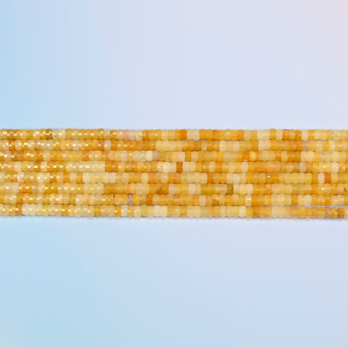 Several strands of Gold Silk Jade faceted heishi disc beads laid in straight rows
