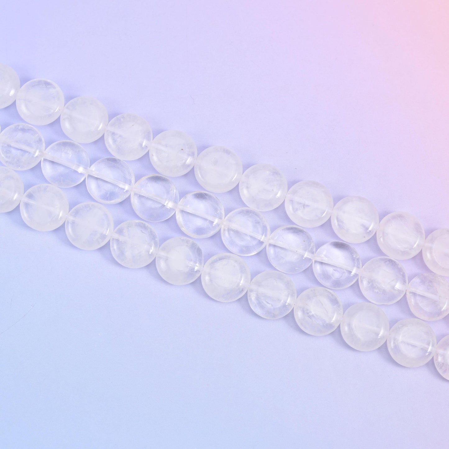 Angled run of clear quartz coins across a soft lavender surface, cloudy and transparent beads mixed