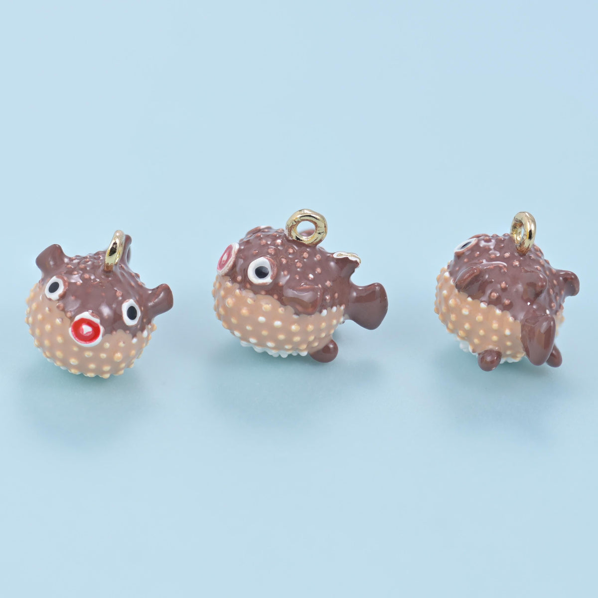 Enamel blowfish charm in chocolate brown with a tan dotted belly, three views of the same plump puffer fish shape.