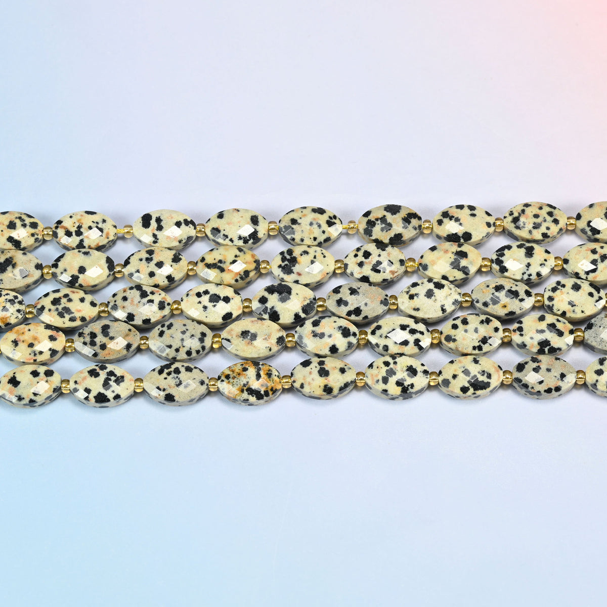 Several strands of dalmatian jasper faceted flat oval beads laid in straight rows with gold seed bead spacers