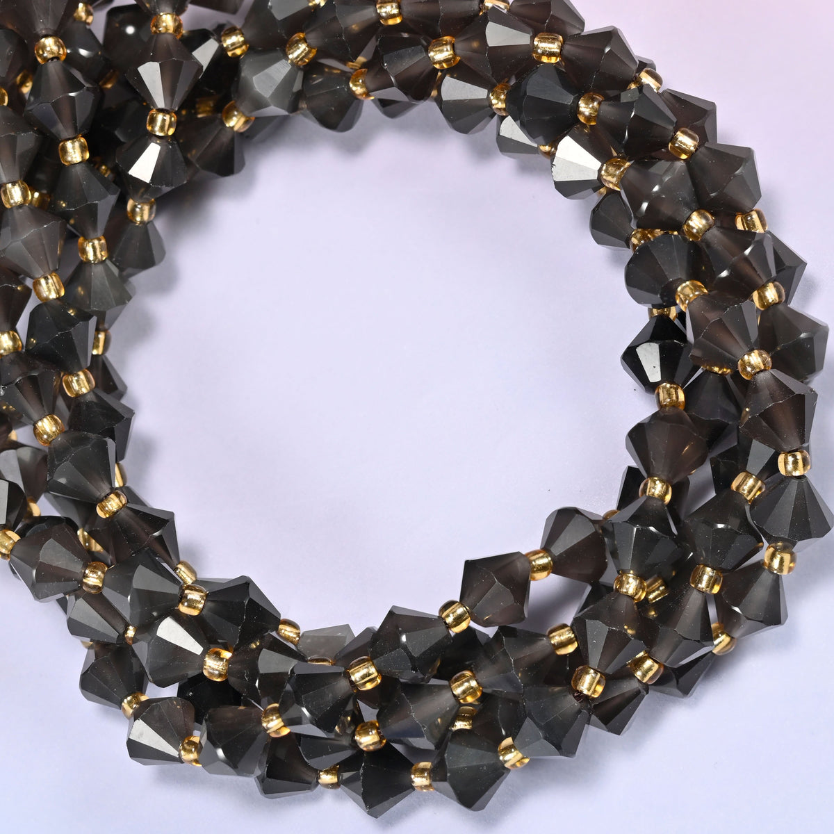 Ice Obsidian faceted bicone beads 8mm with gold-tone spacers, strand coiled into a tighter circle, close-up view