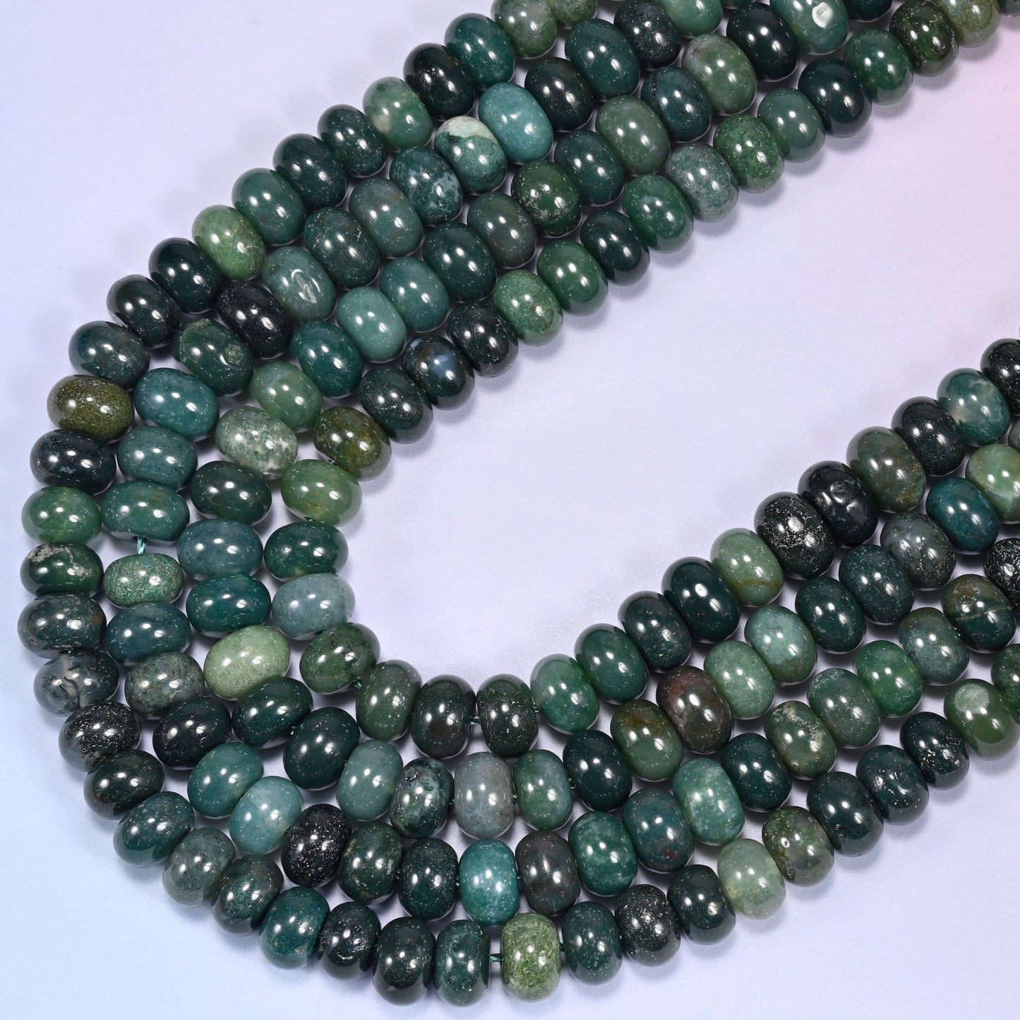 Circular coil of Moss Agate bead strands on a lavender background.