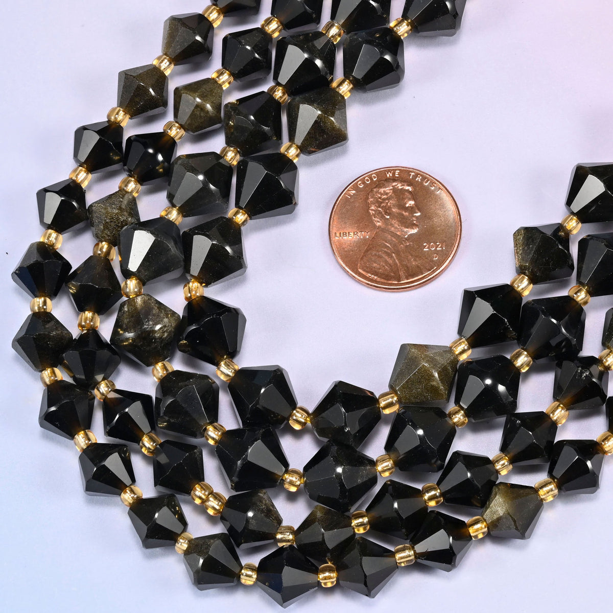 Ice Obsidian faceted bicone beads 8mm with gold-tone spacers, strand coiled into a loose loop with a penny alongside for scale