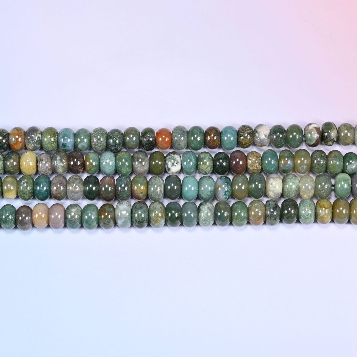 Overhead view of several rows of Indian Agate rondelle beads showing the multicolor green and rust patterning on a light lavender surface.