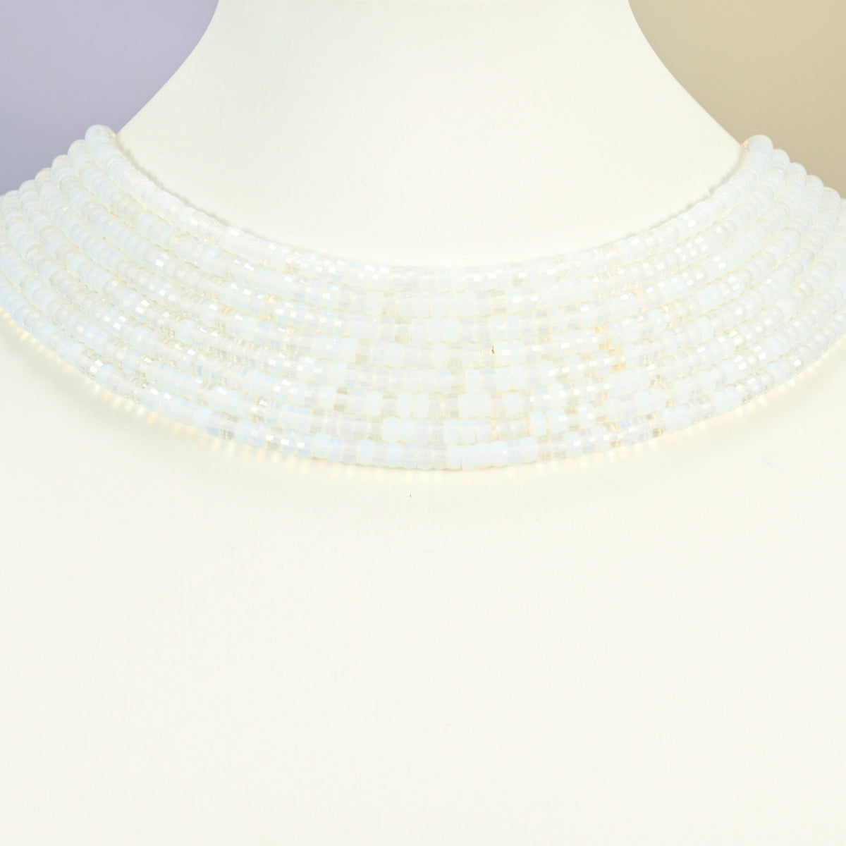 Opalite faceted heishi disc strands arranged as a layered collar on a white display bust, milky white beads across the neck