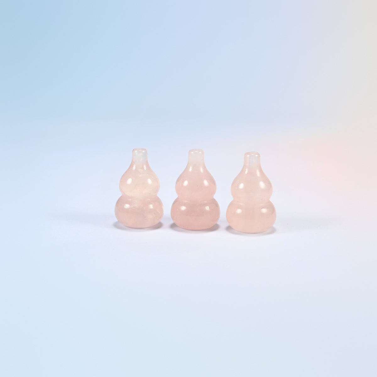 Three 1.2 inch natural rose quartz gourd crystal carvings standing in a row, light pink