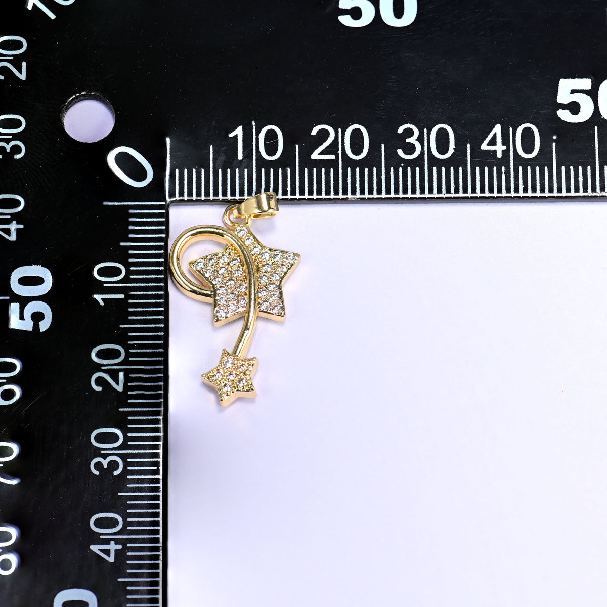 Wishing star zirconia charm against a black millimetre ruler, the gold shooting star pendant measuring roughly 25mm tall.
