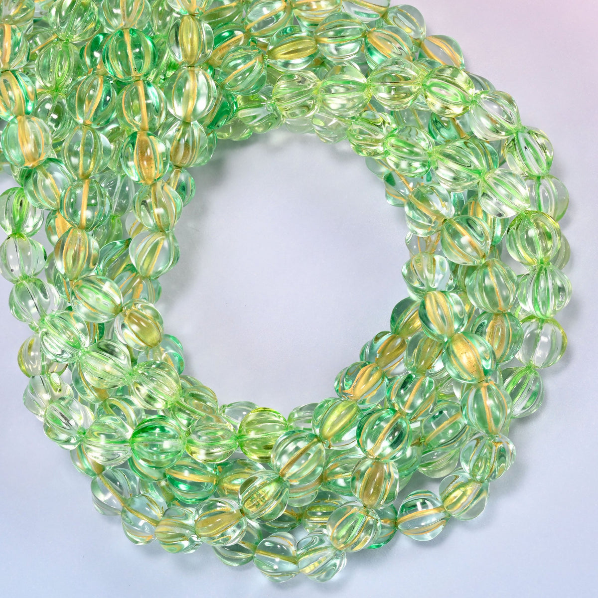 Green gold pumpkin glass beads coiled with the open center to one side, showing the fluted grooves end on.