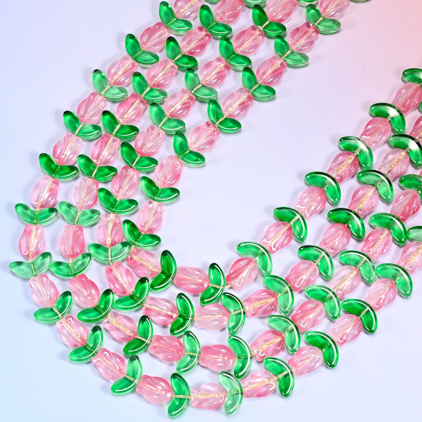 Close-up of tulip and leaf glass bead strands coiled in a tight spiral pattern on a lavender background.