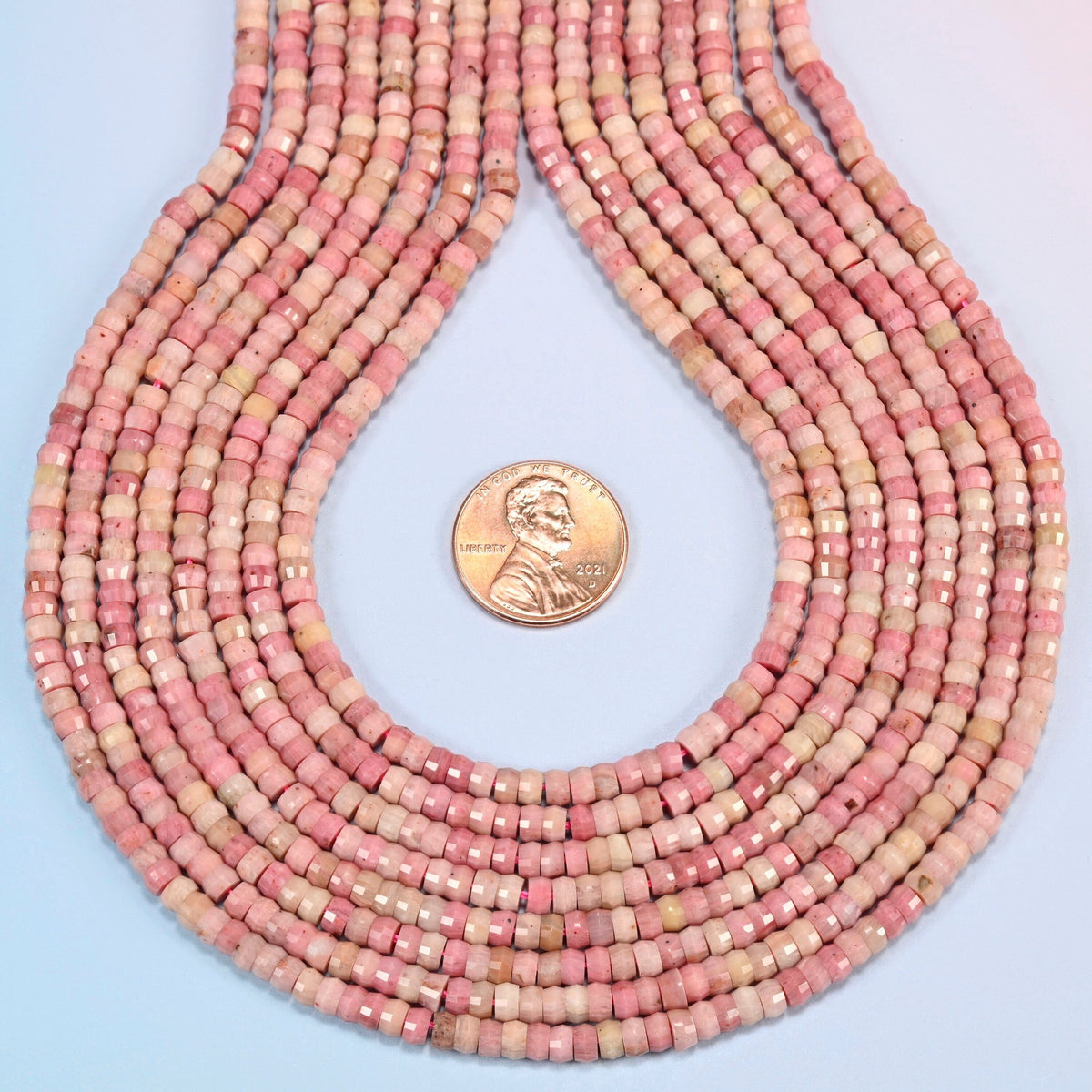 Pink rhodonite faceted heishi disc strands formed into a teardrop loop around a US penny for scale