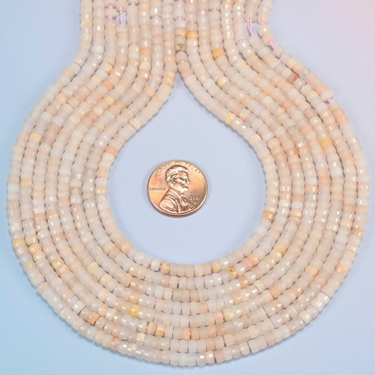 Pink aventurine faceted heishi disc strands formed into a teardrop loop around a US penny for scale