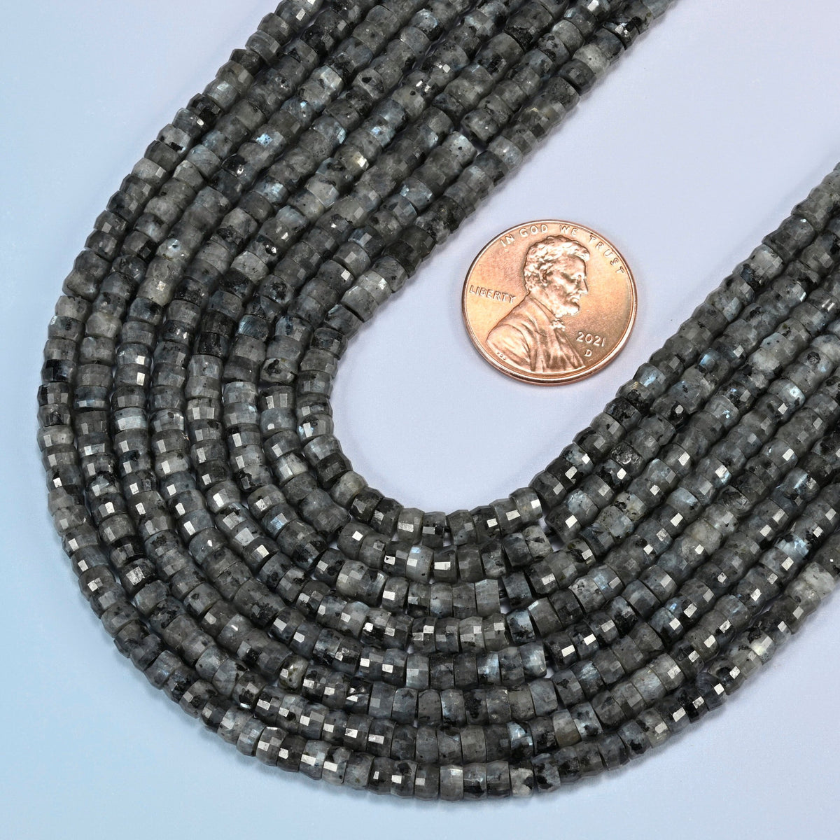 Close view of black labradorite faceted heishi disc strands curving beside a US penny for scale