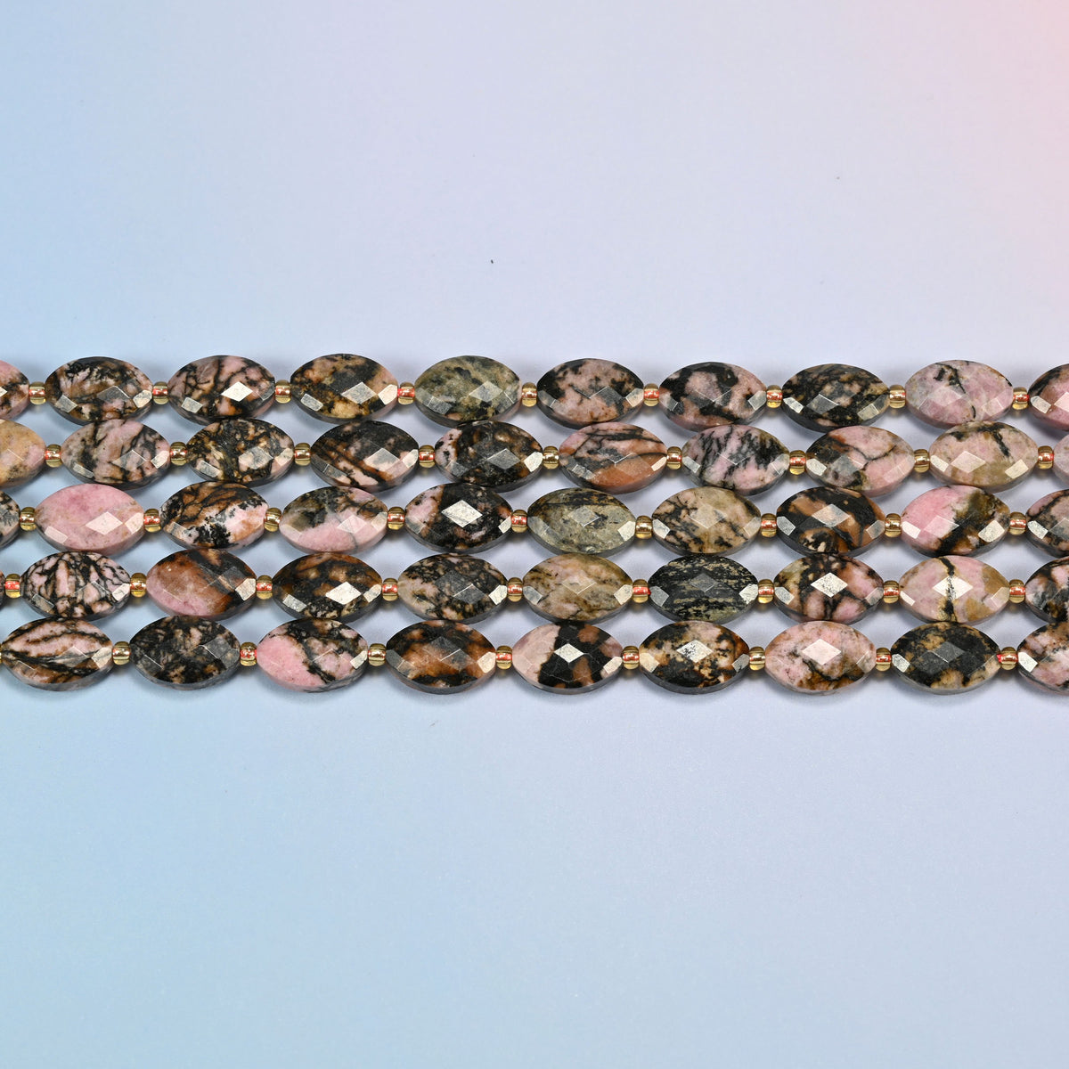 Several strands of rhodonite faceted flat oval beads laid in straight rows with gold seed bead spacers
