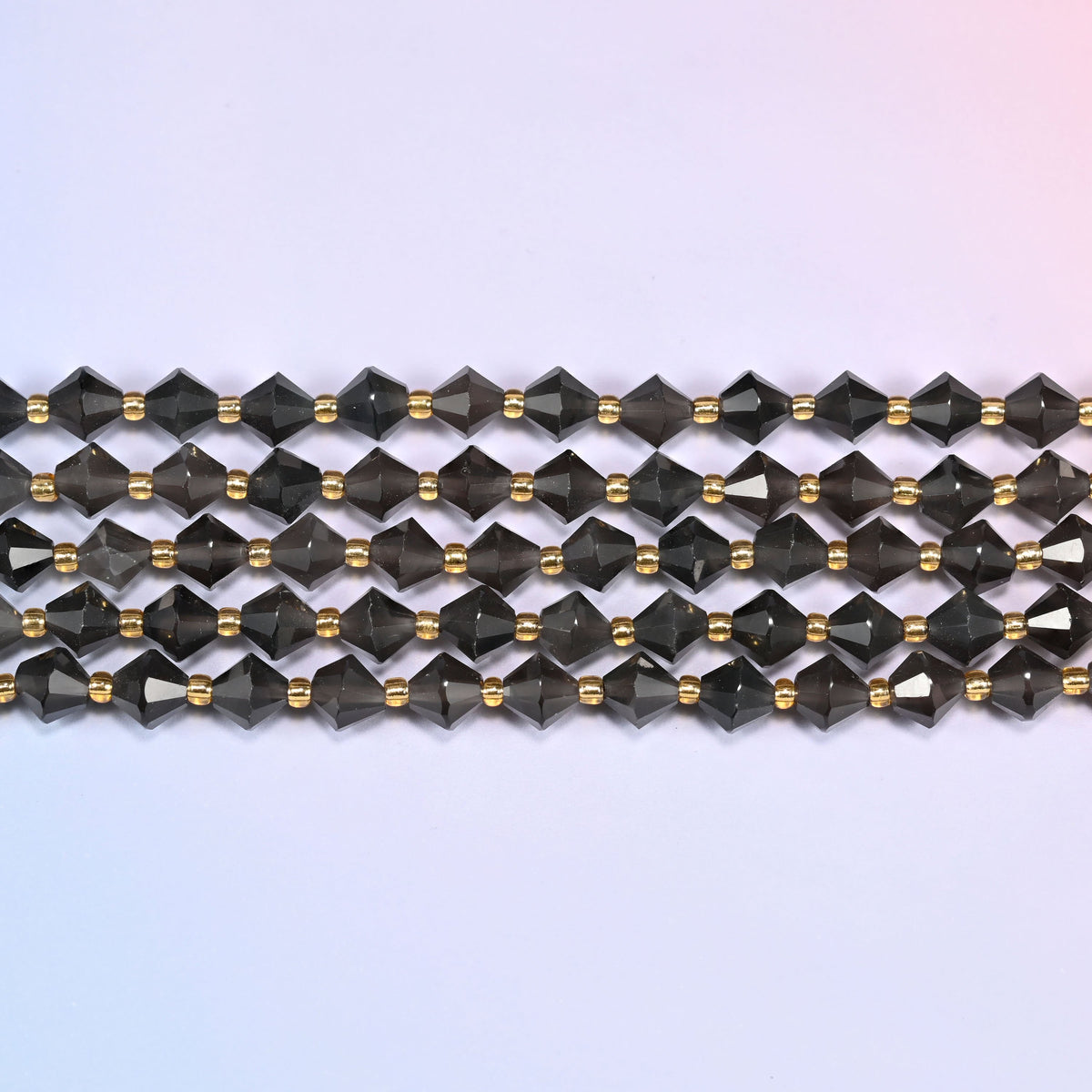 Ice Obsidian faceted bicone beads 8mm with gold-tone spacers, strand laid straight in a wide view showing the beaded texture