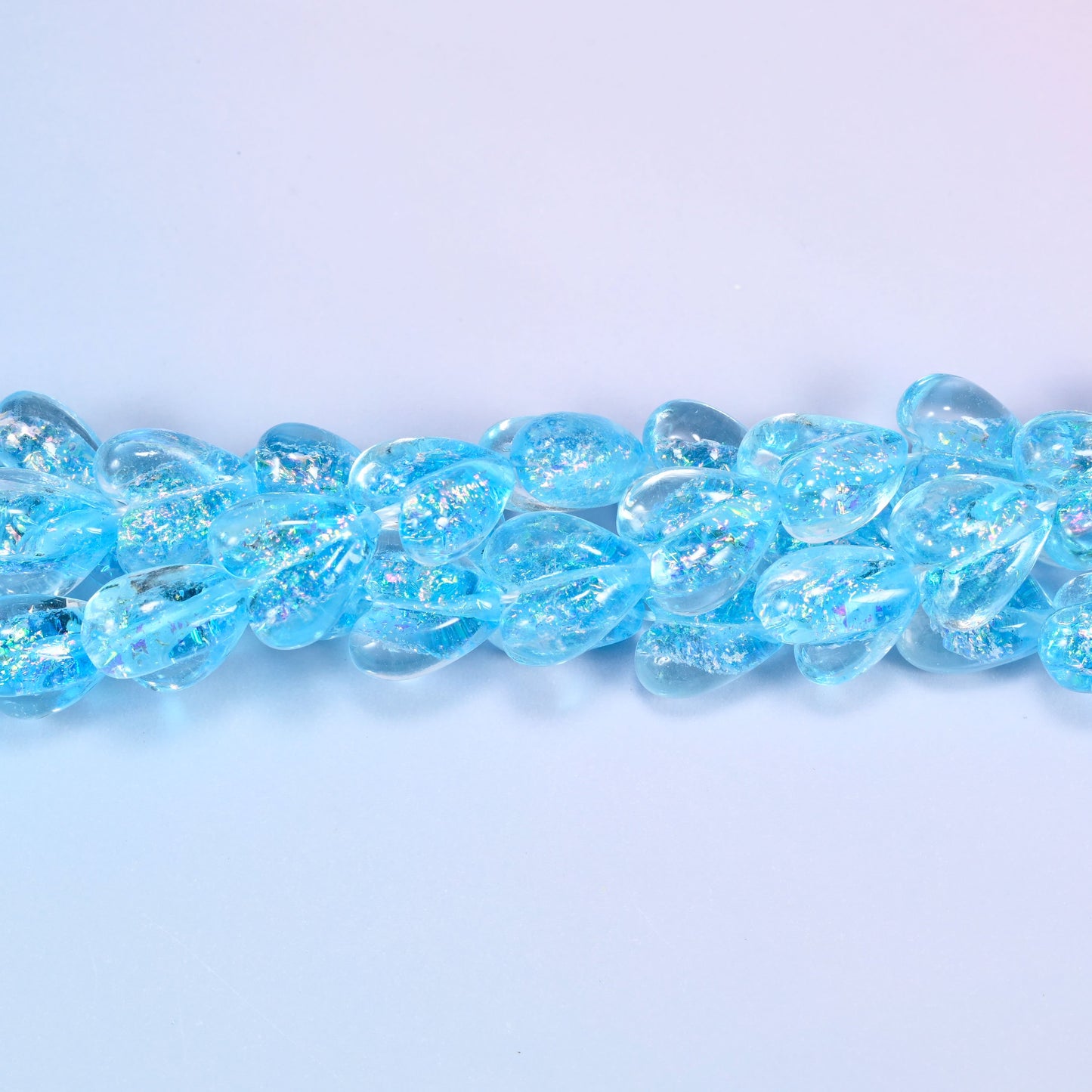 Iridescent light blue heart glass beads in a close straight row, showing the even moulded heart shape