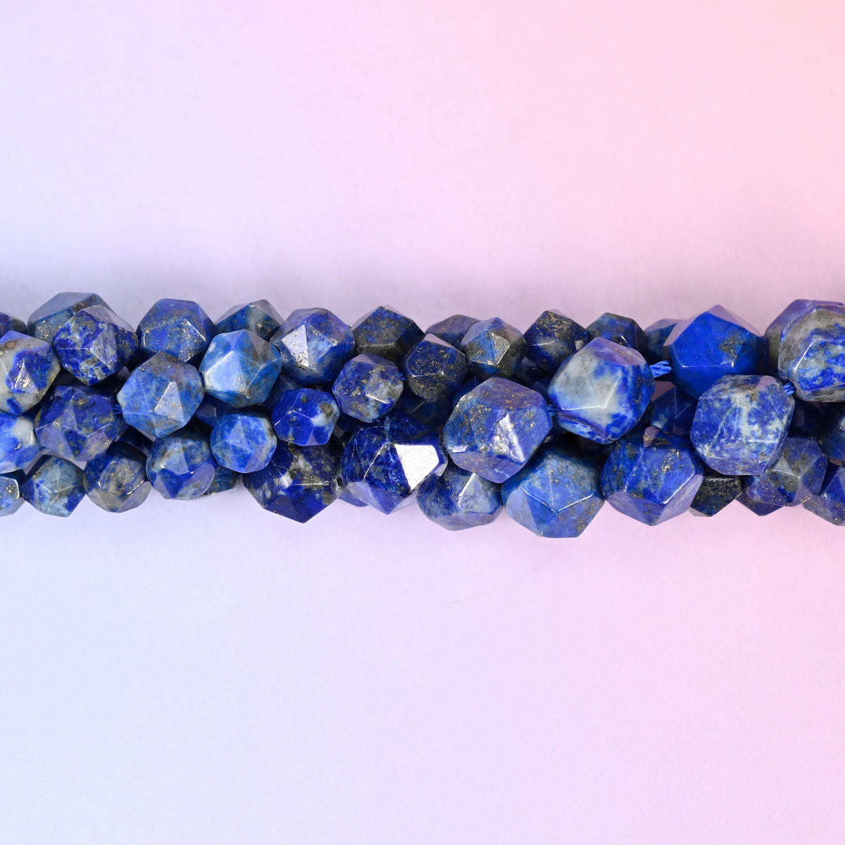 Blue Lapis Lazuli faceted beads close up in a single row, flat triangular star cut planes with small gold pyrite flecks