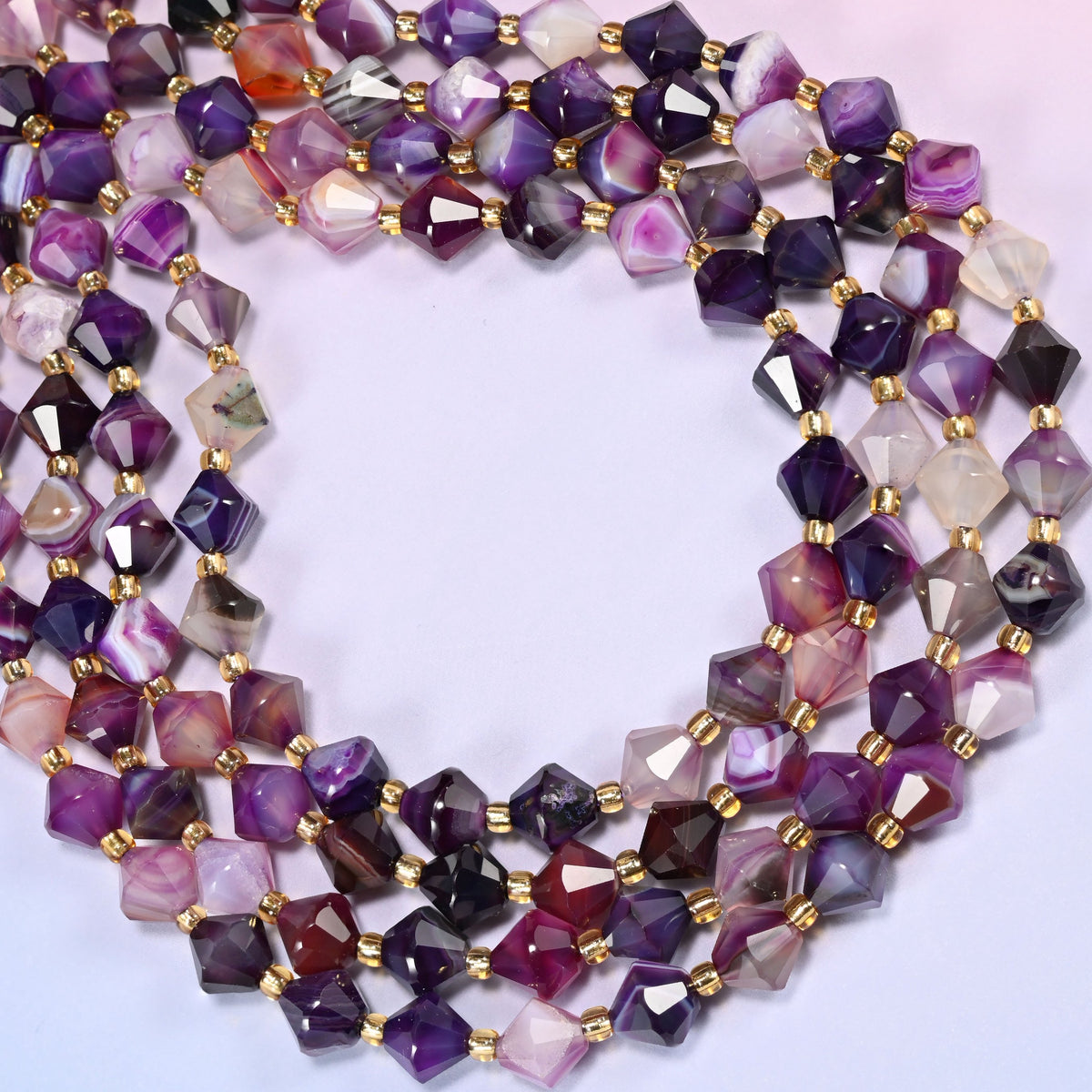 8mm Dyed Purple Strip Agate faceted bicone beads coiled into a loose circle on a light lavender background.