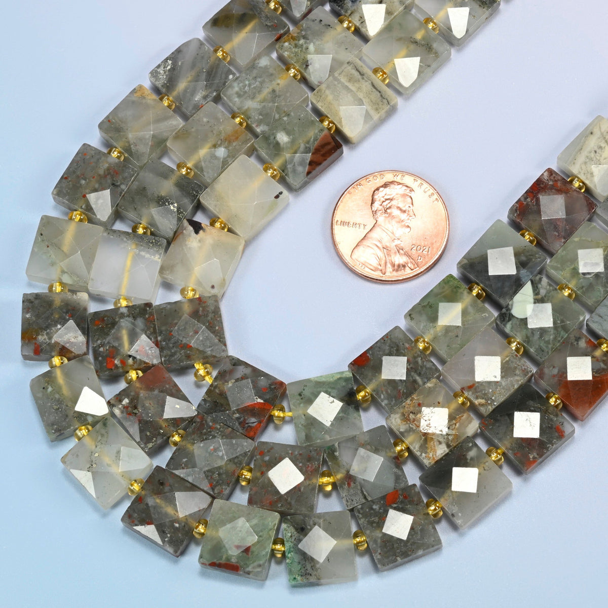 Close view of natural African bloodstone faceted flat square strands curving beside a US penny for scale