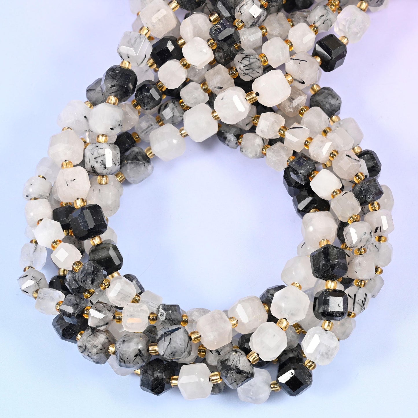 Frosted white and clear quartz cubes with cut corners, each one crossed by black rutile needles - a few beads almost solid graphite, most veiled and smoky, some nearly clear.
