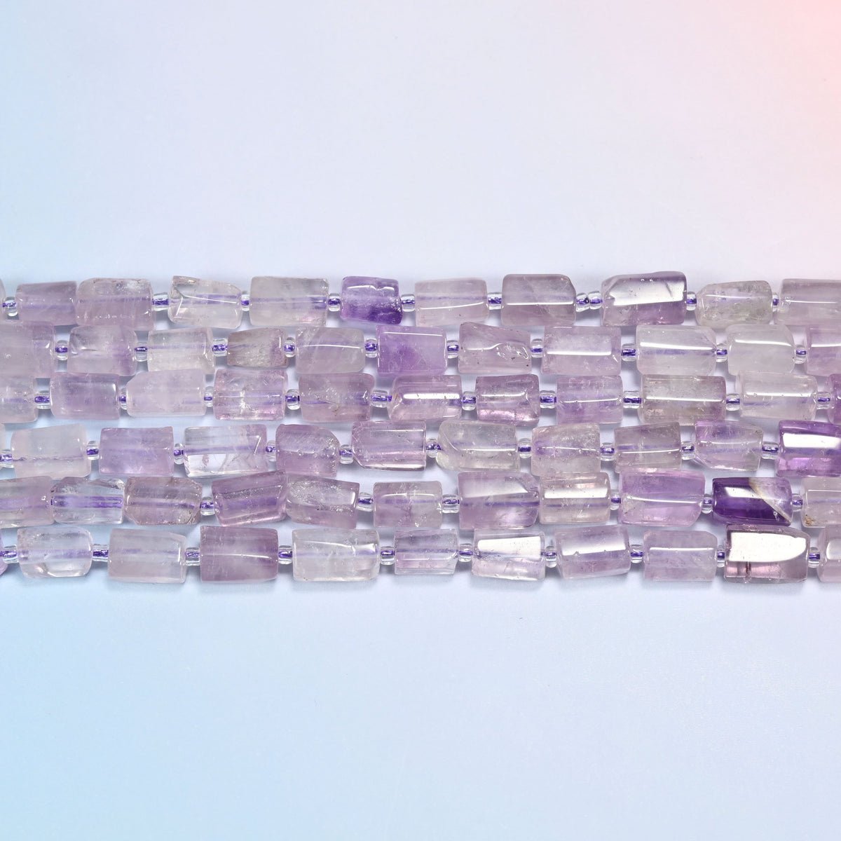 Lavender amethyst faceted tube beads laid in straight horizontal rows with tiny clear glass seed bead spacers on violet thread.