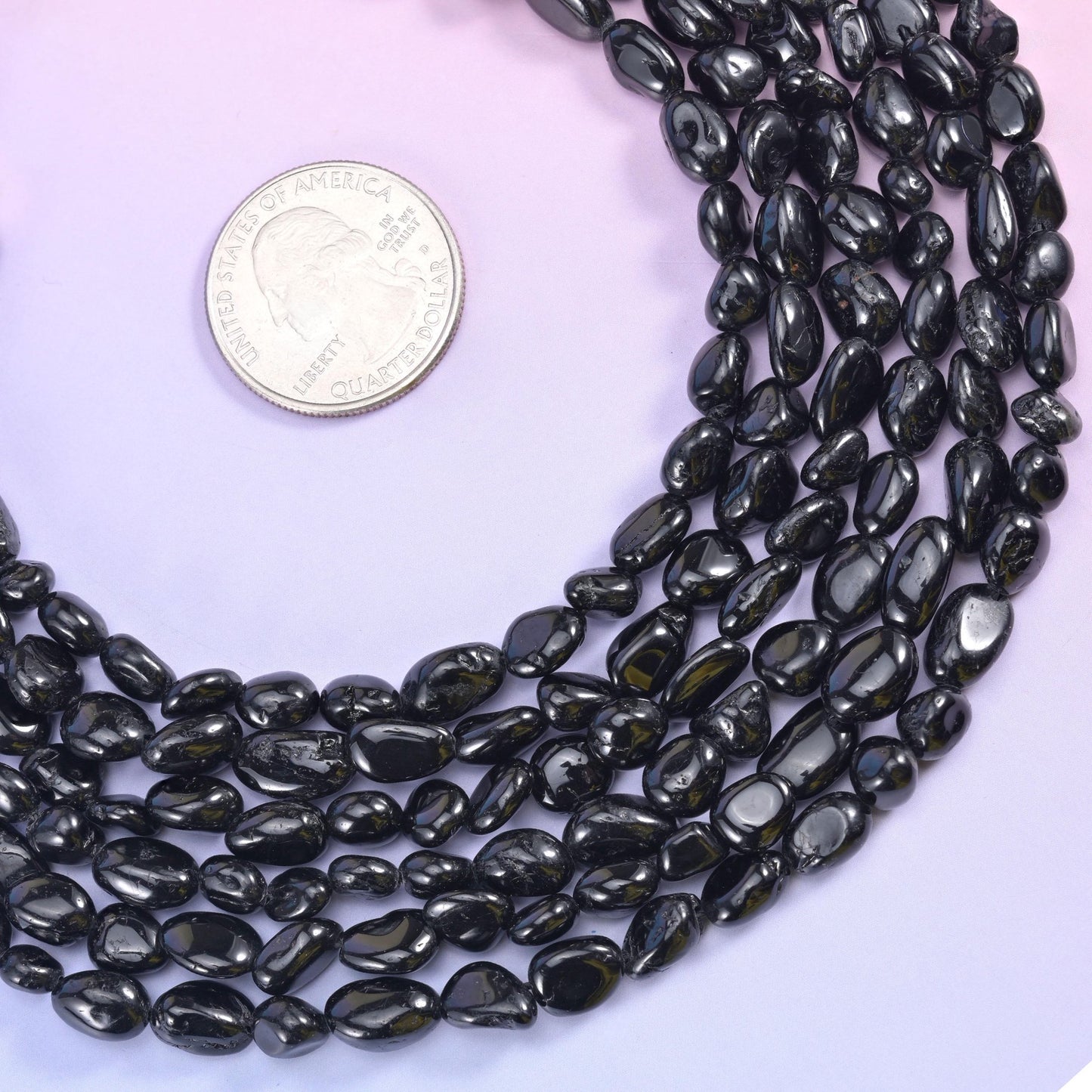 Black tourmaline strand coiled beside a silver coin, showing the 6-8mm bead range