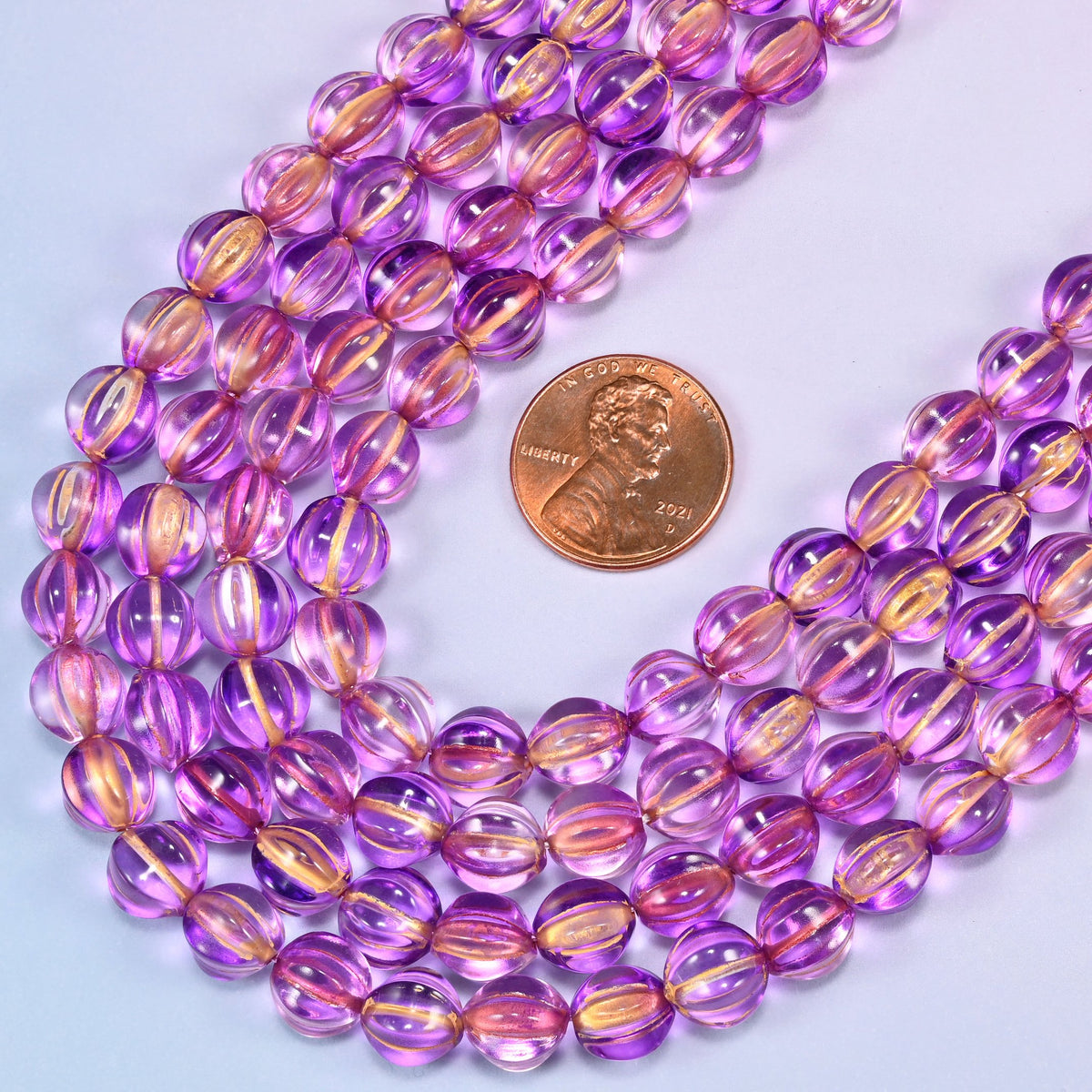 Purple gold pumpkin glass beads coiled loosely, shown with a US penny resting on the strands for scale.