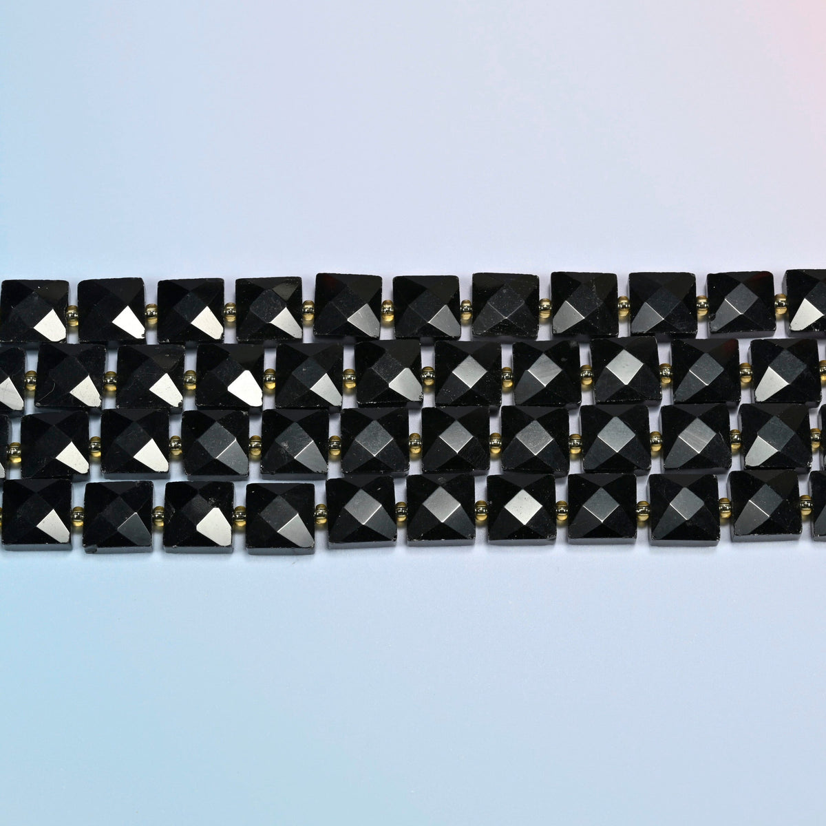 Several strands of natural black onyx faceted flat square beads laid in straight rows